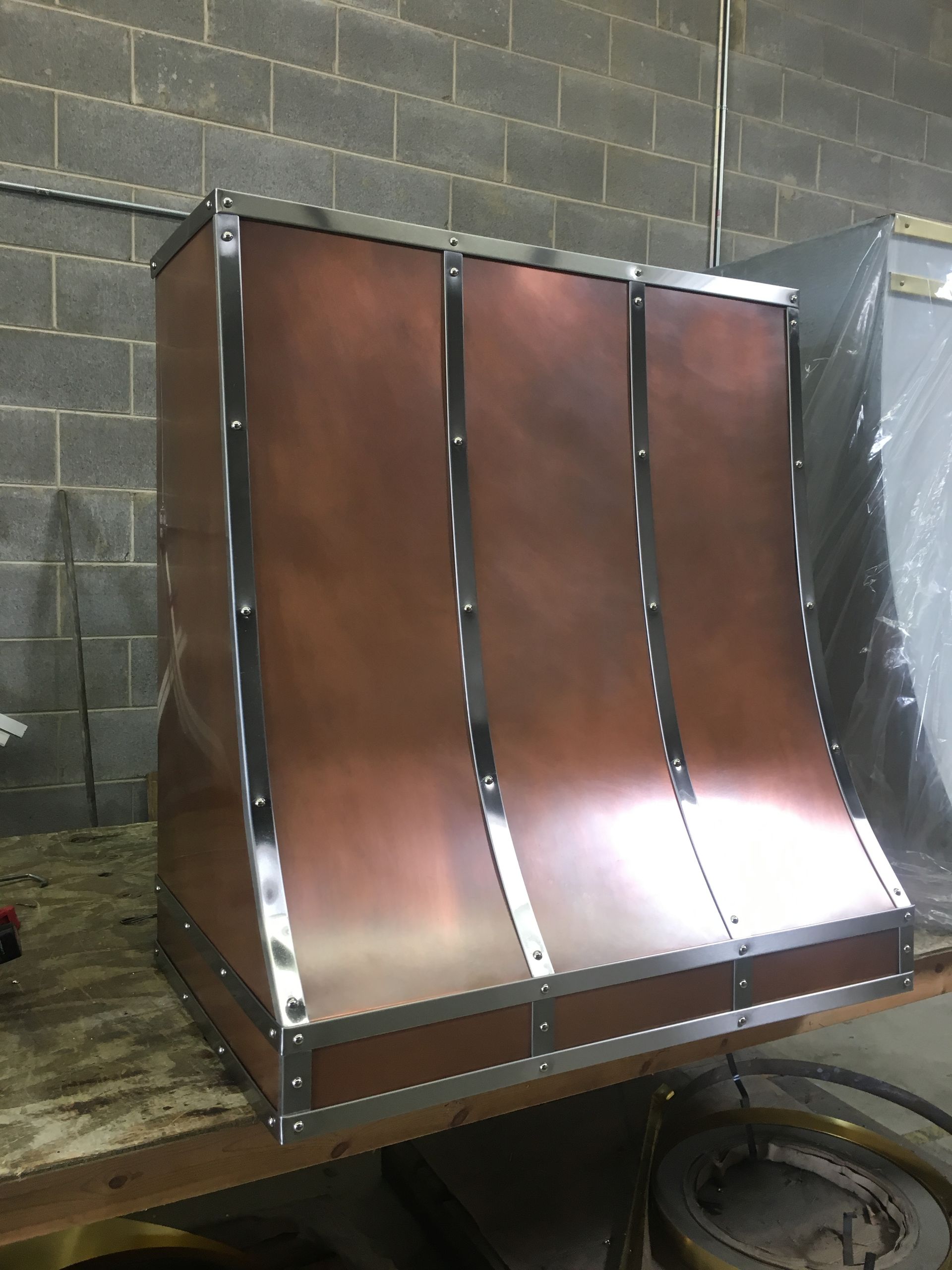 A copper hood is sitting on a wooden table in front of a brick wall.