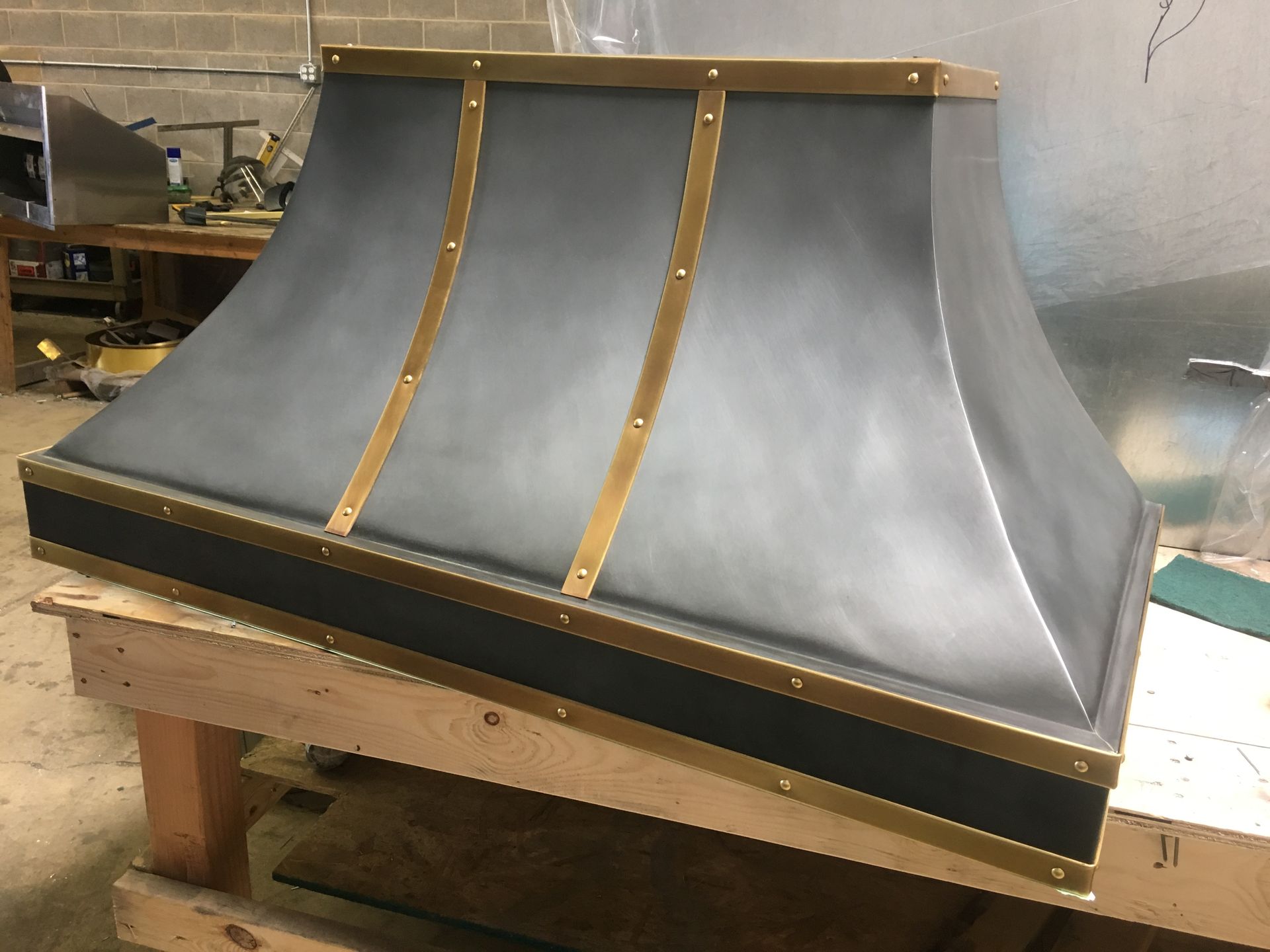A metal hood with brass trim is sitting on a wooden table.