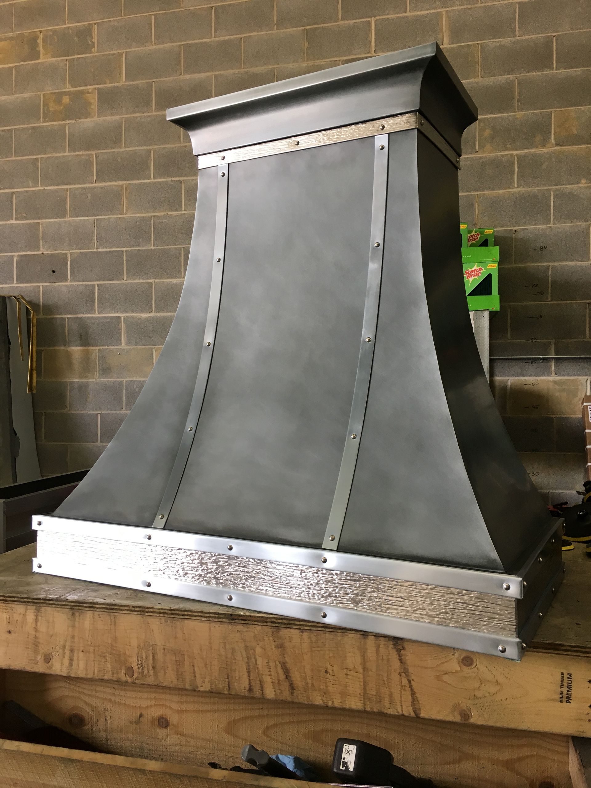 A metal hood is sitting on top of a wooden table in front of a brick wall.