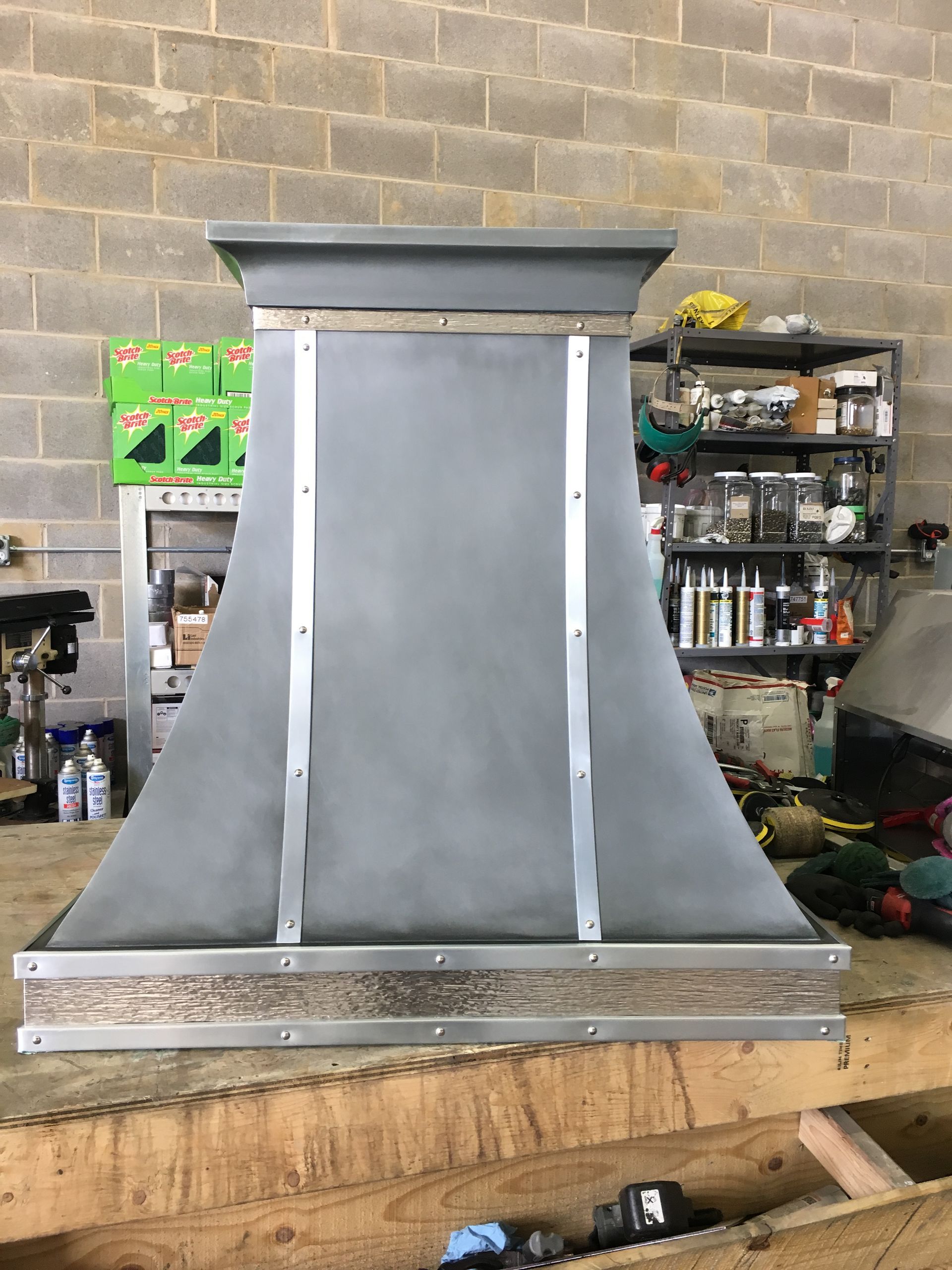 A metal hood is sitting on top of a wooden table in a garage.