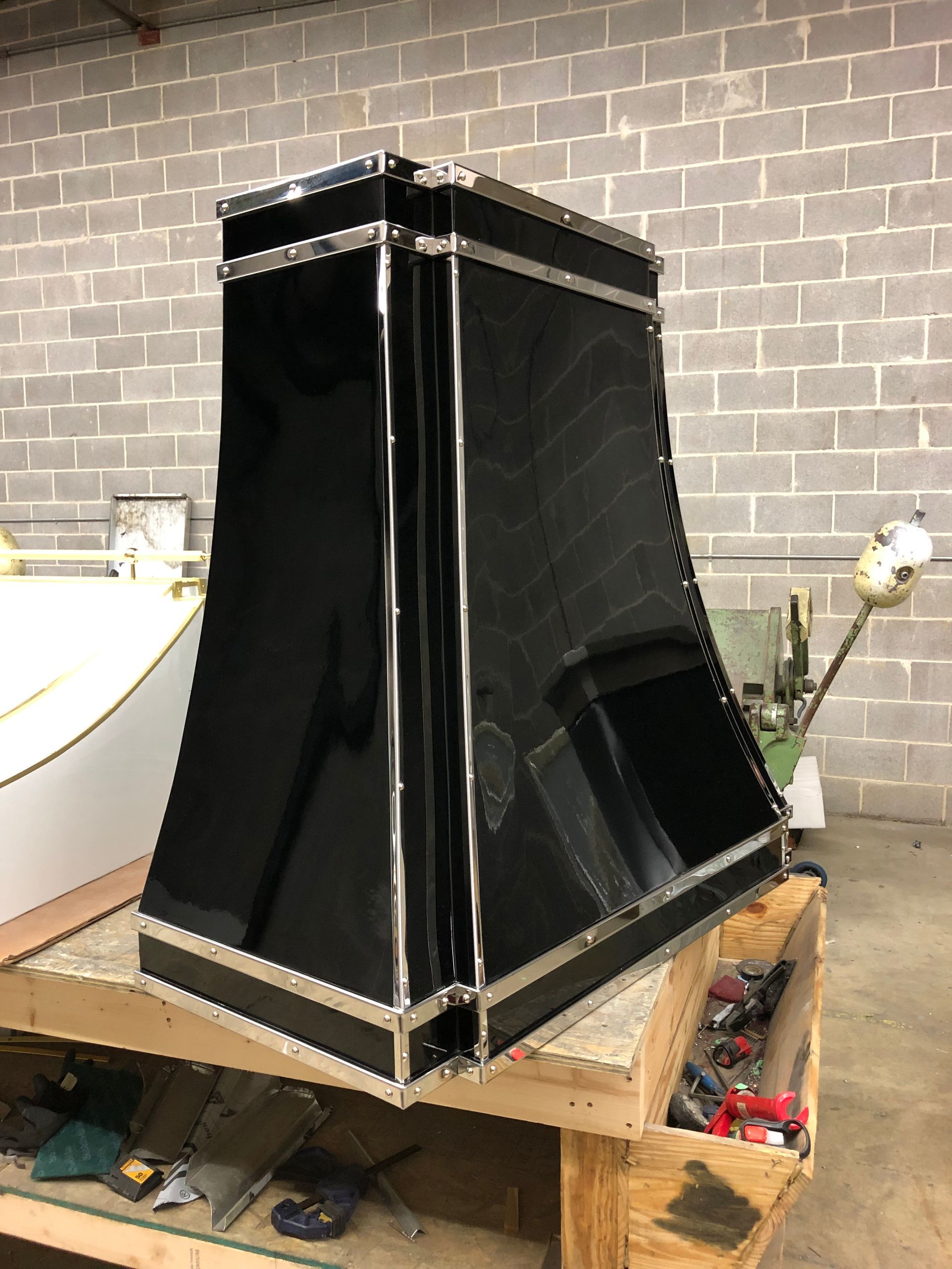 A black hood is sitting on top of a wooden table in front of a brick wall.