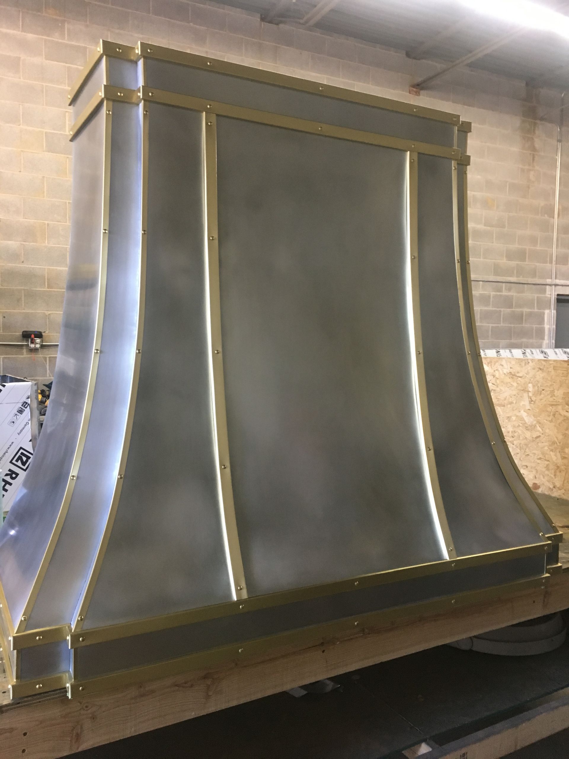 A stainless steel hood with brass trim is sitting on a wooden table.