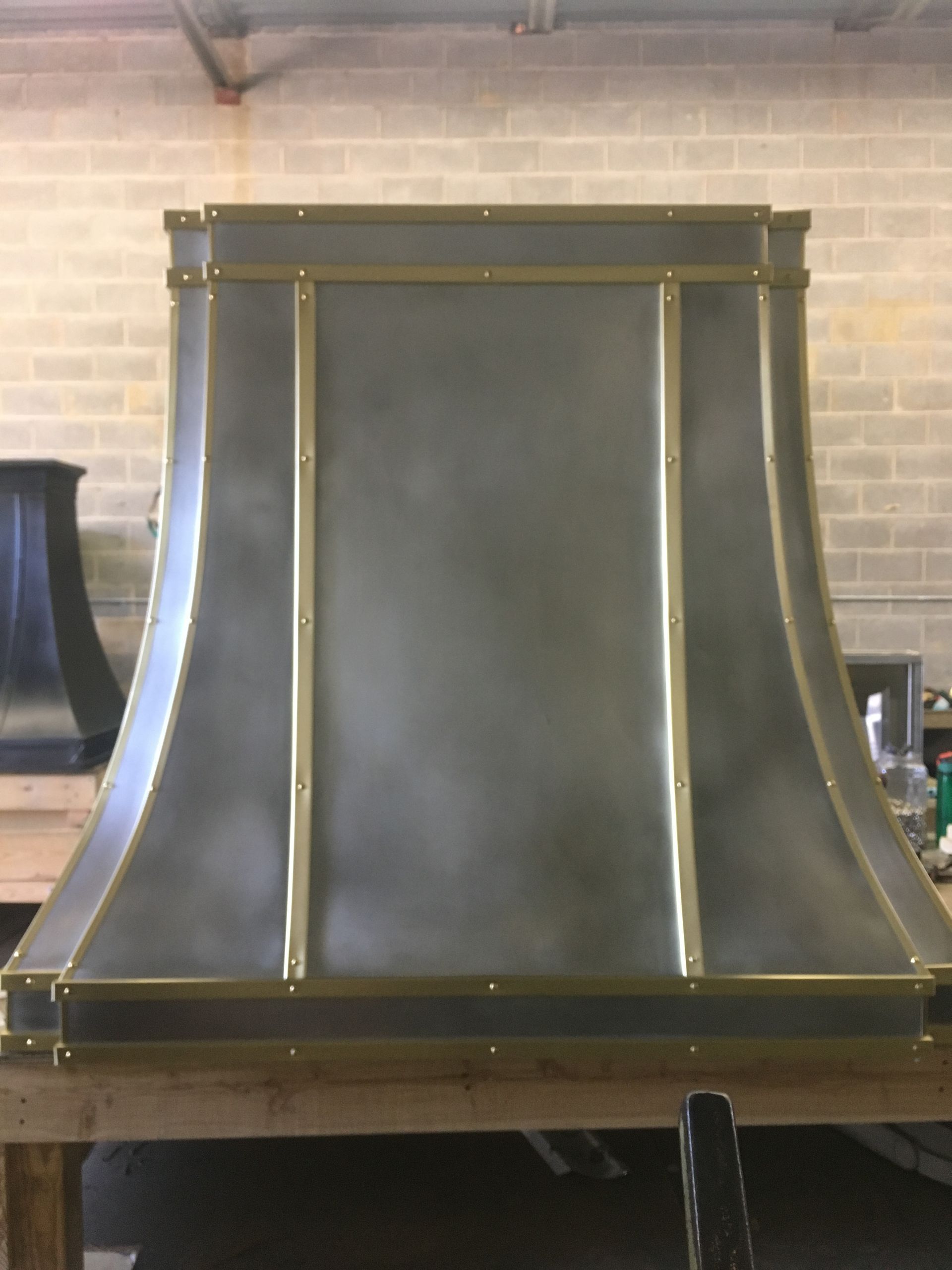 A stainless steel hood with brass trim is sitting on top of a wooden table.
