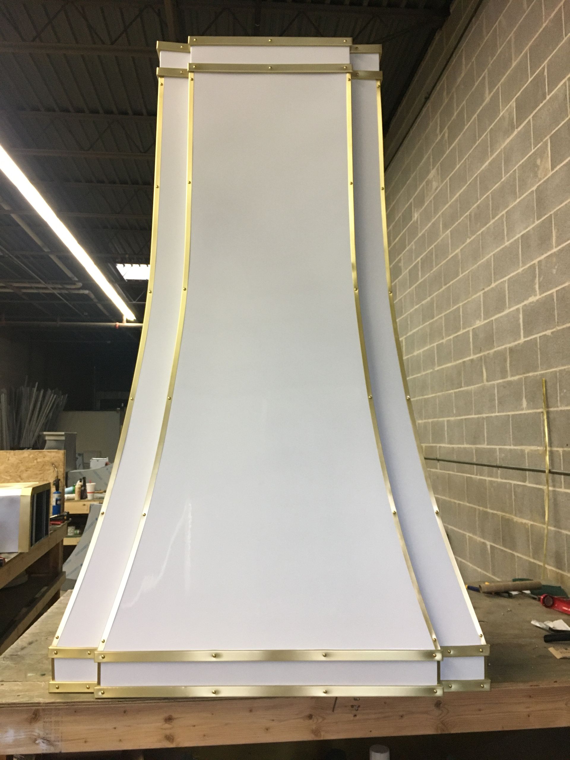 A white hood with gold trim is sitting on a wooden table in front of a brick wall.