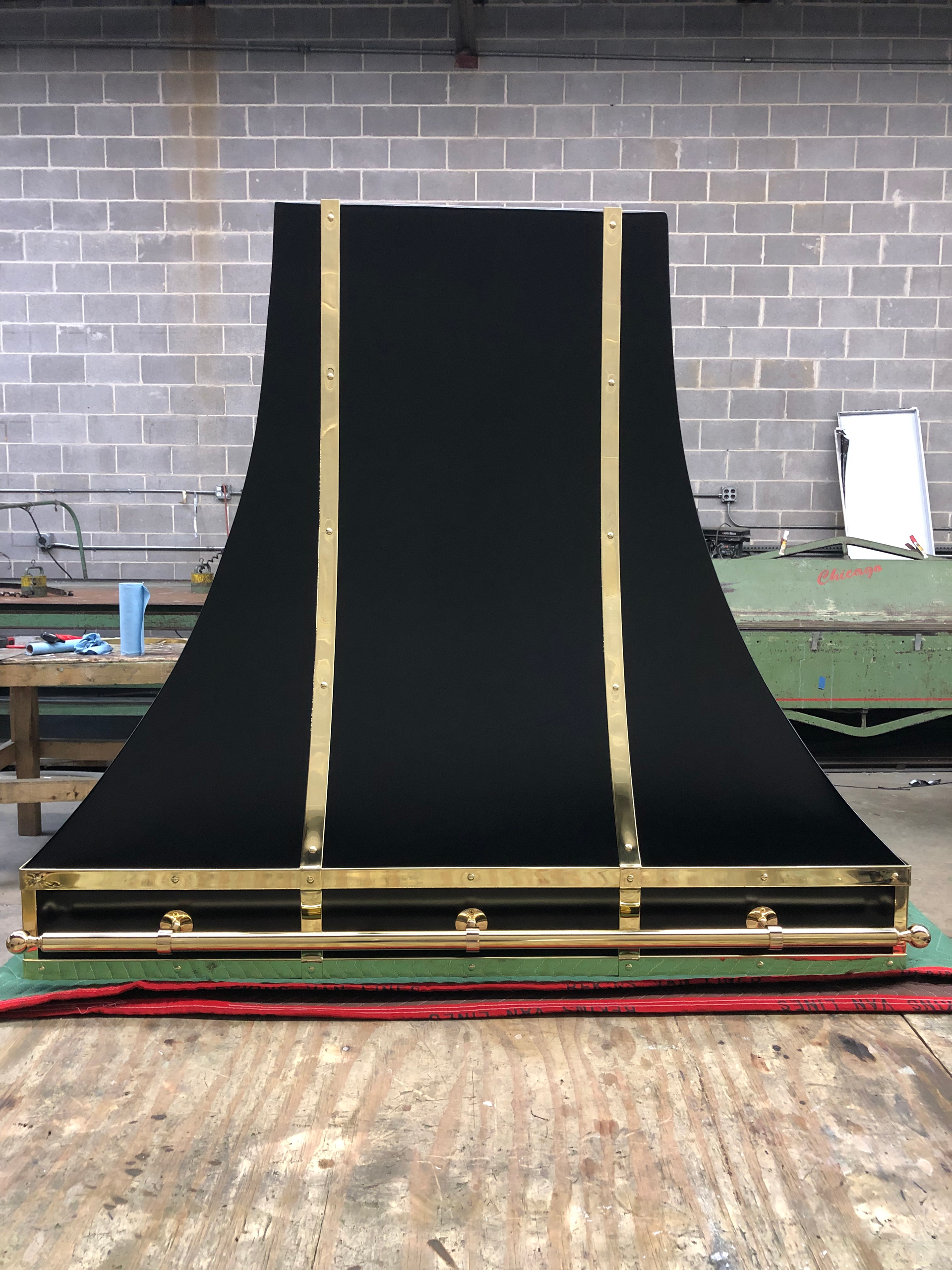 A black and gold hood is sitting on a wooden table in front of a brick wall.