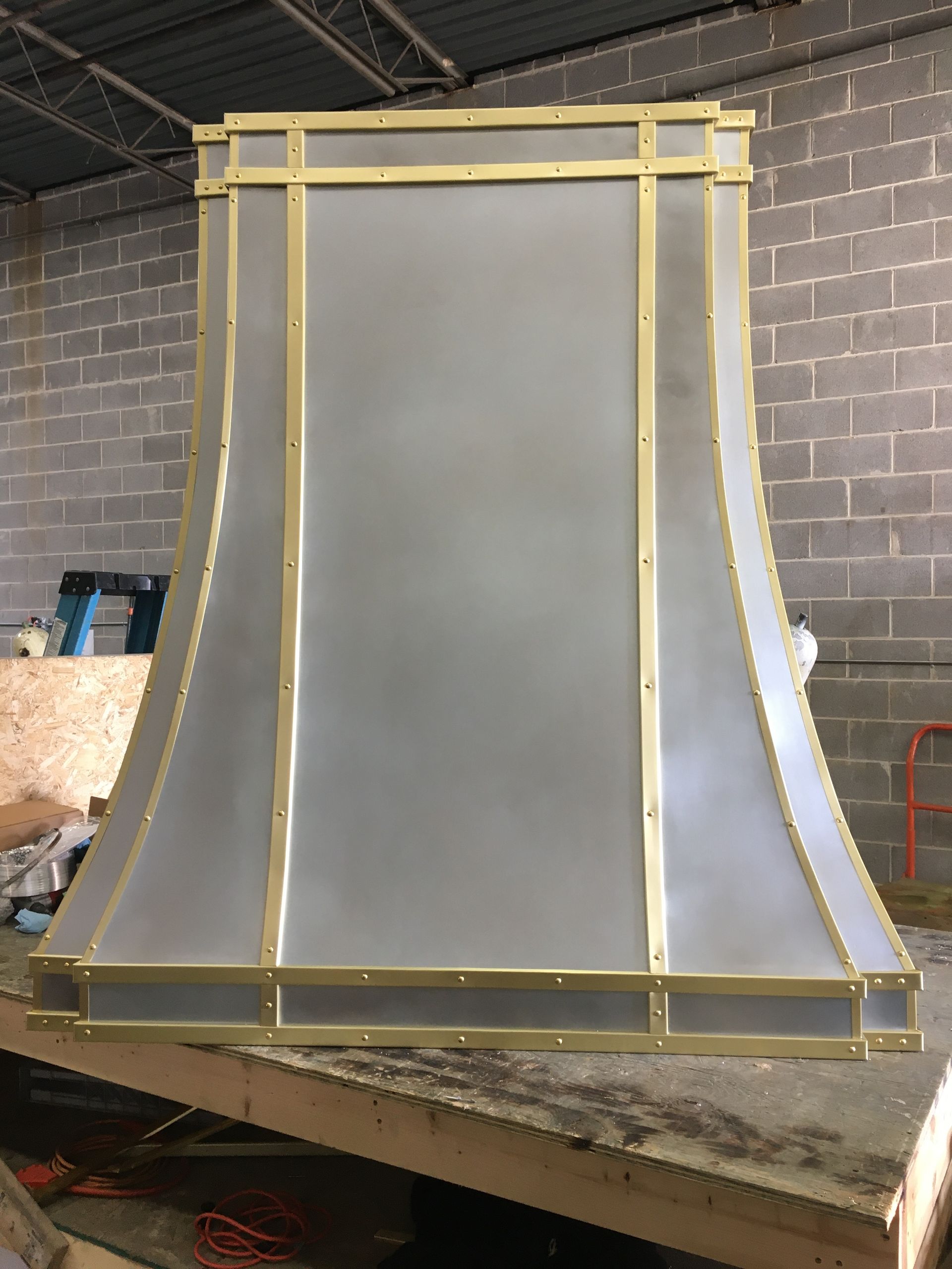 A stainless steel hood with brass trim is sitting on top of a wooden table.