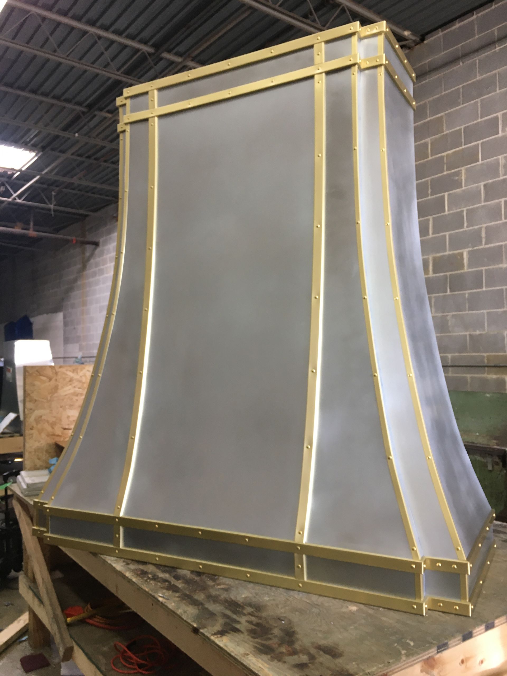 A stainless steel hood with brass trim is sitting on top of a wooden table.