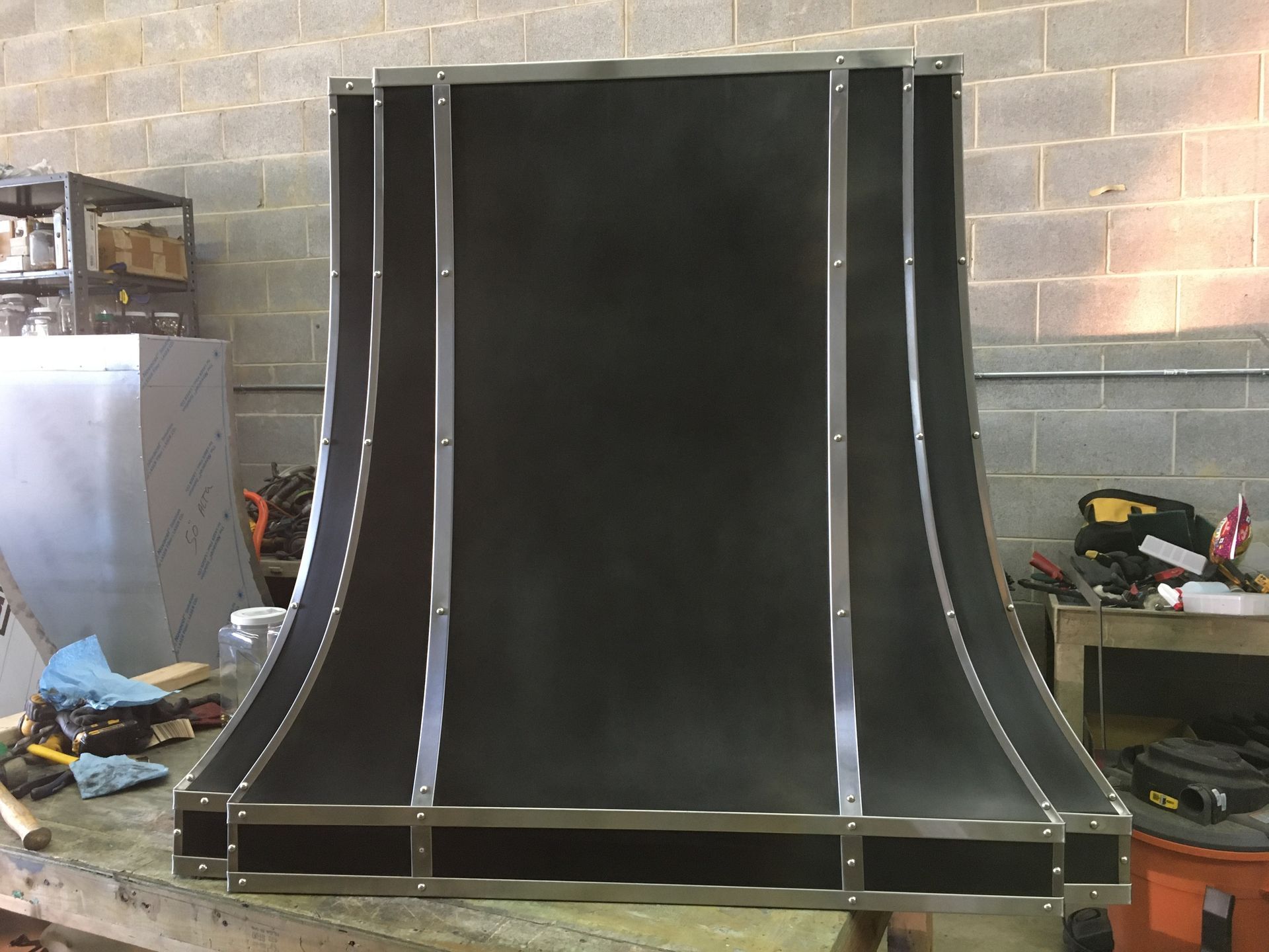 A black hood is sitting on a wooden table in front of a brick wall.