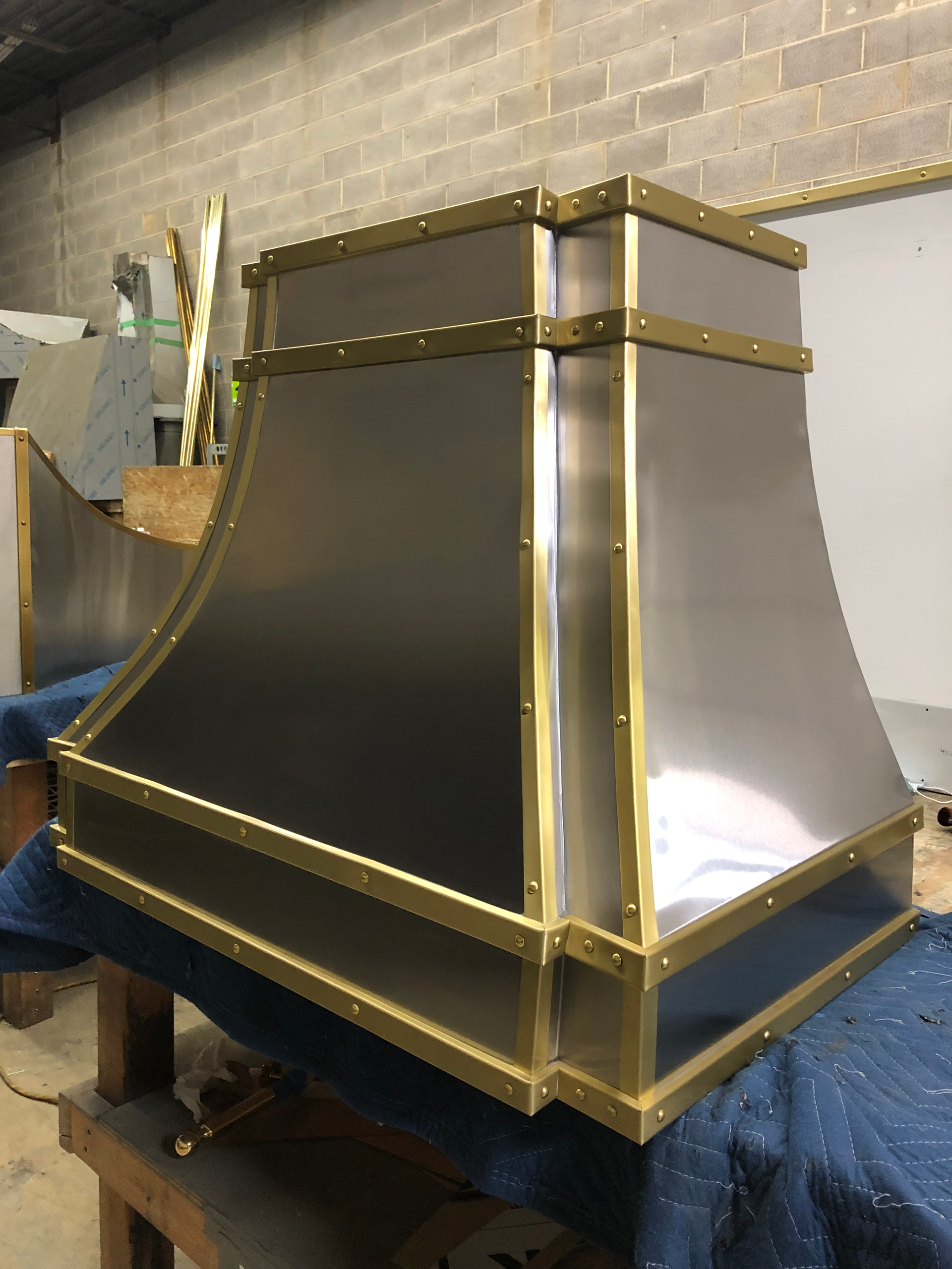 A stainless steel hood with brass trim is sitting on a wooden table.
