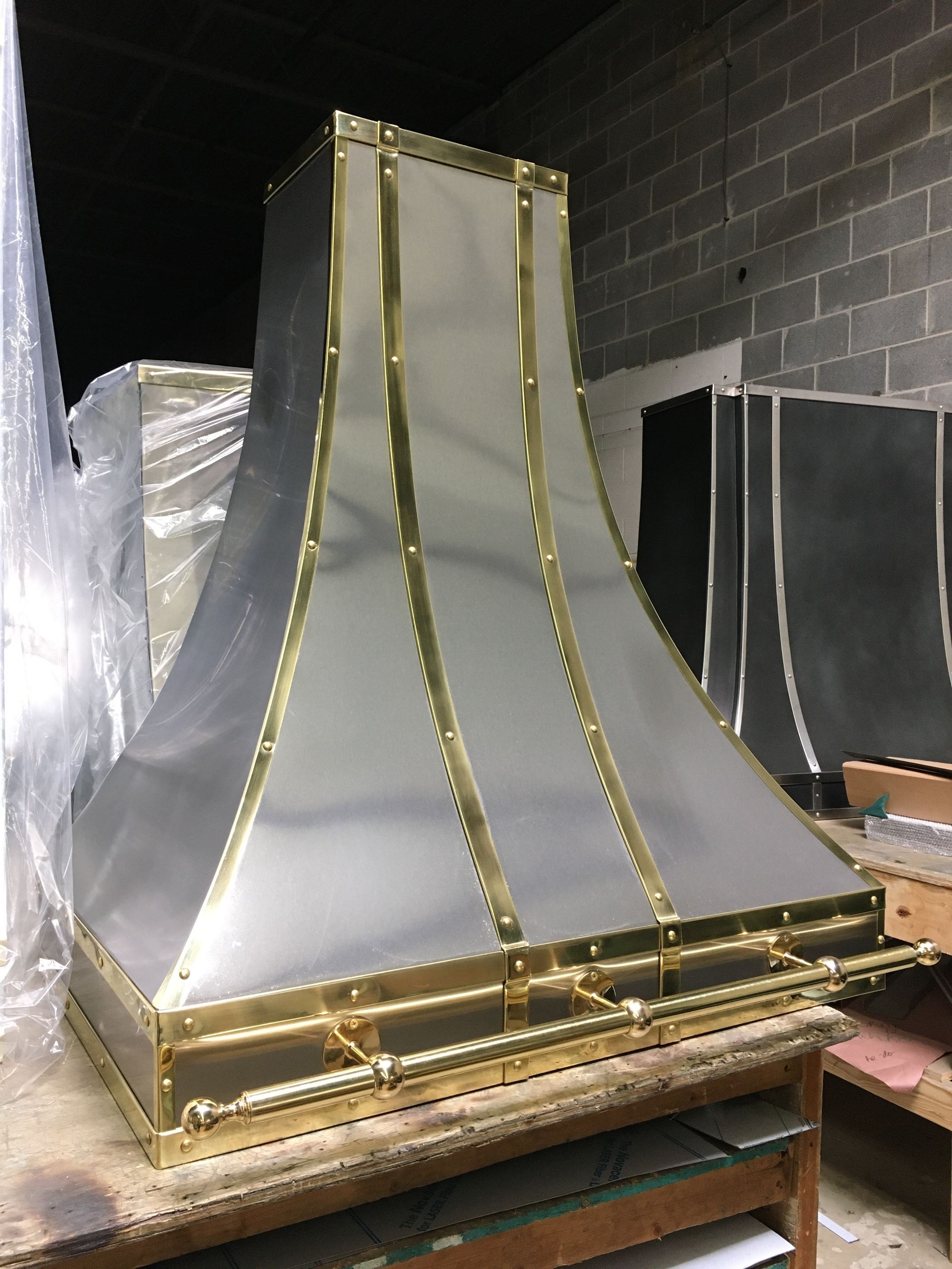 A stainless steel hood with brass trim is sitting on a wooden table.