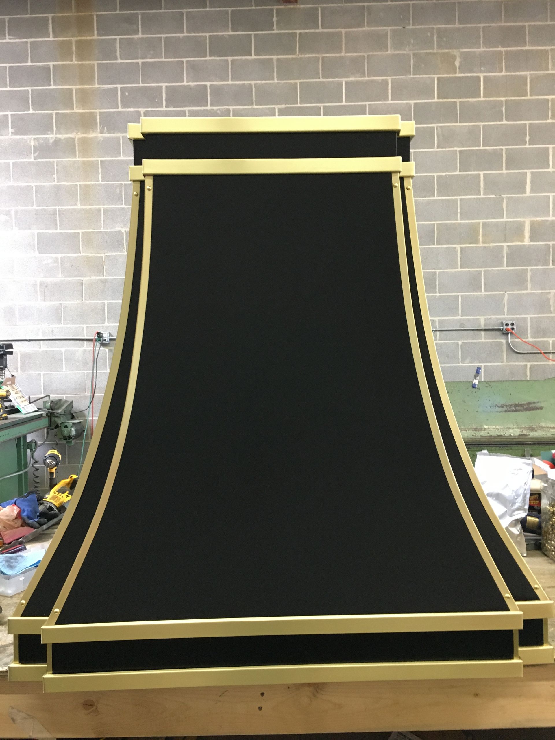 A black and gold hood is sitting on a wooden table in front of a brick wall.