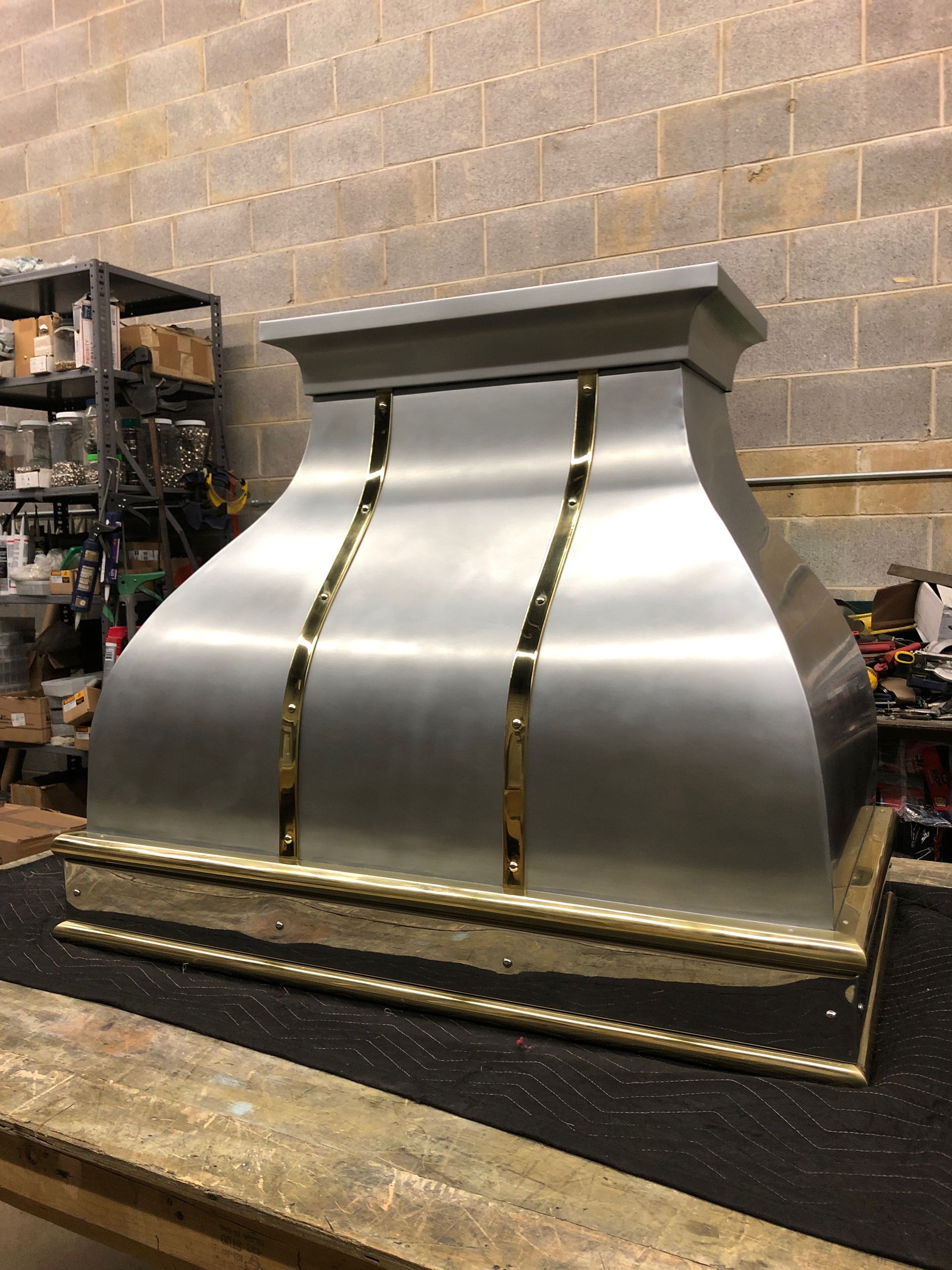 A stainless steel hood with gold trim is sitting on a wooden table.