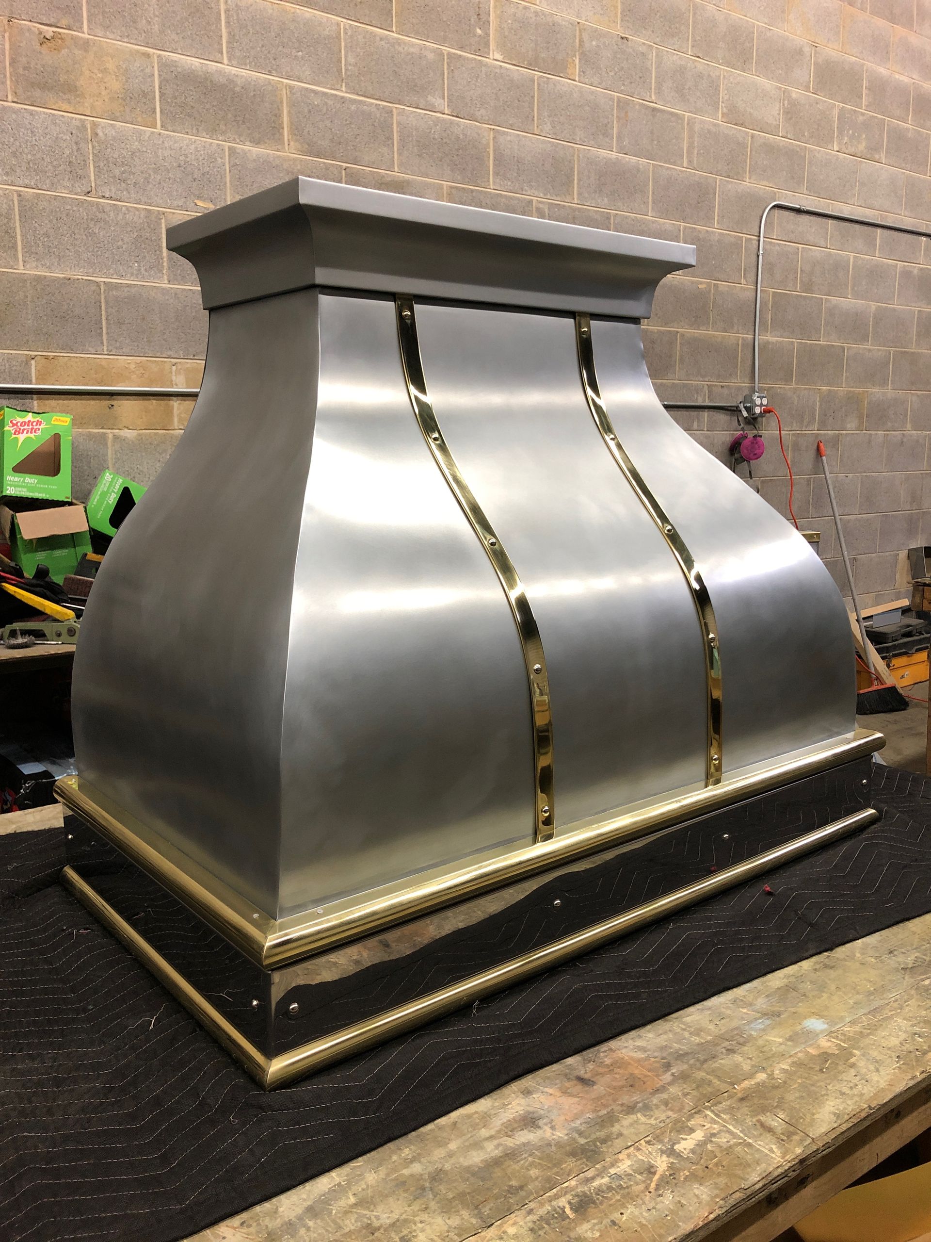 A stainless steel hood with gold trim is sitting on a wooden table.