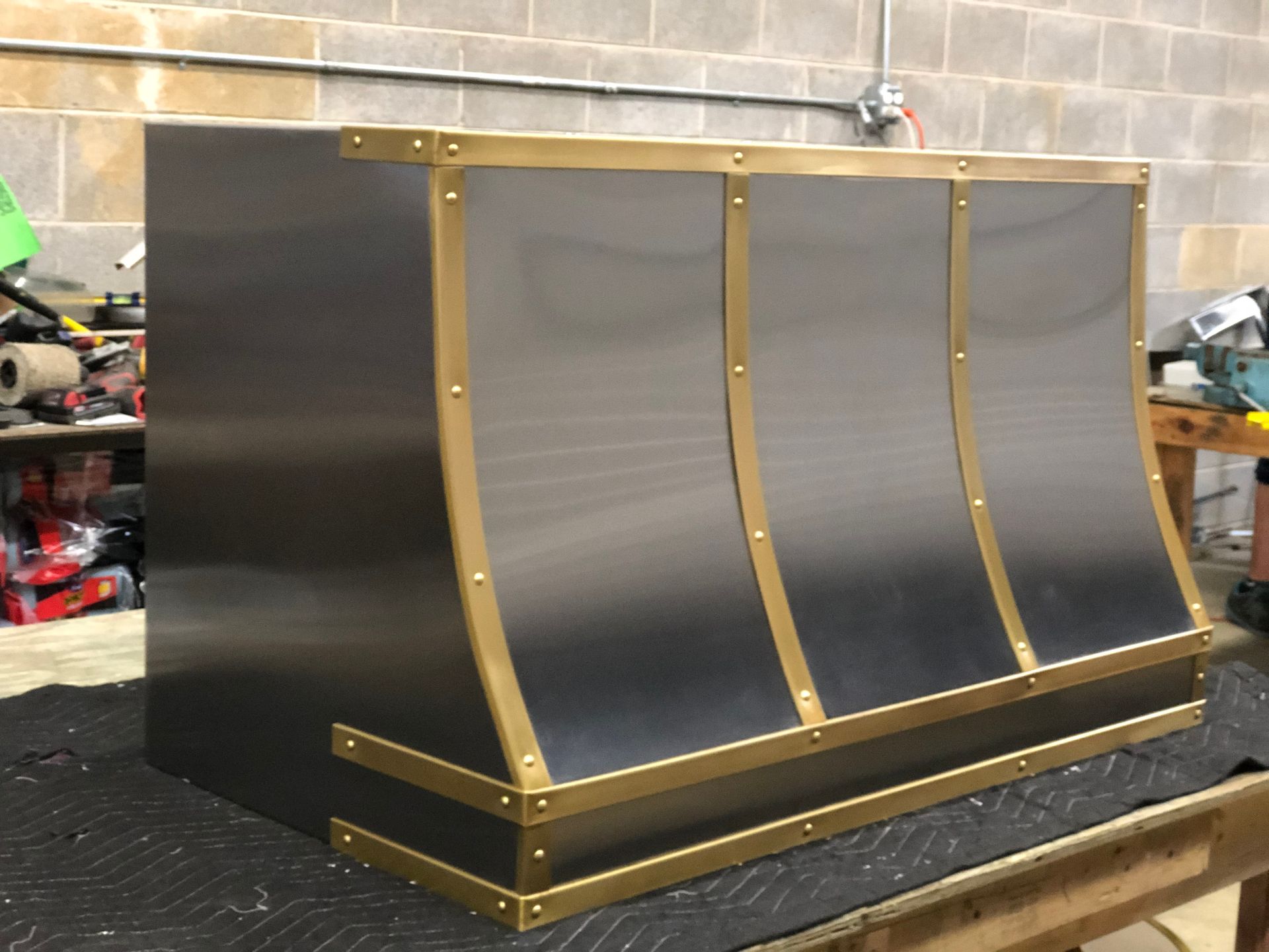A stainless steel hood with brass trim is sitting on a table.