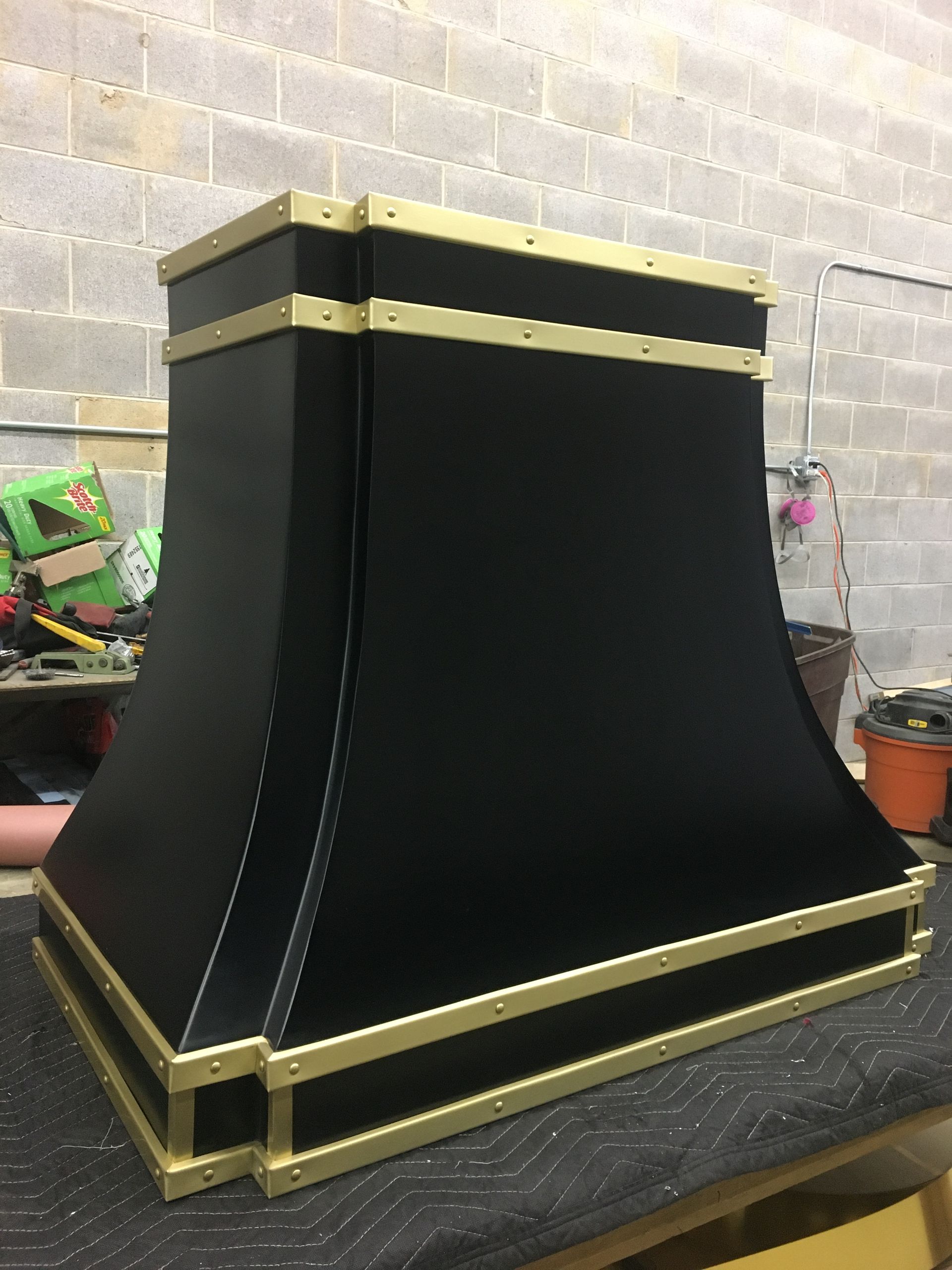 A black and gold hood is sitting on a table in front of a brick wall.