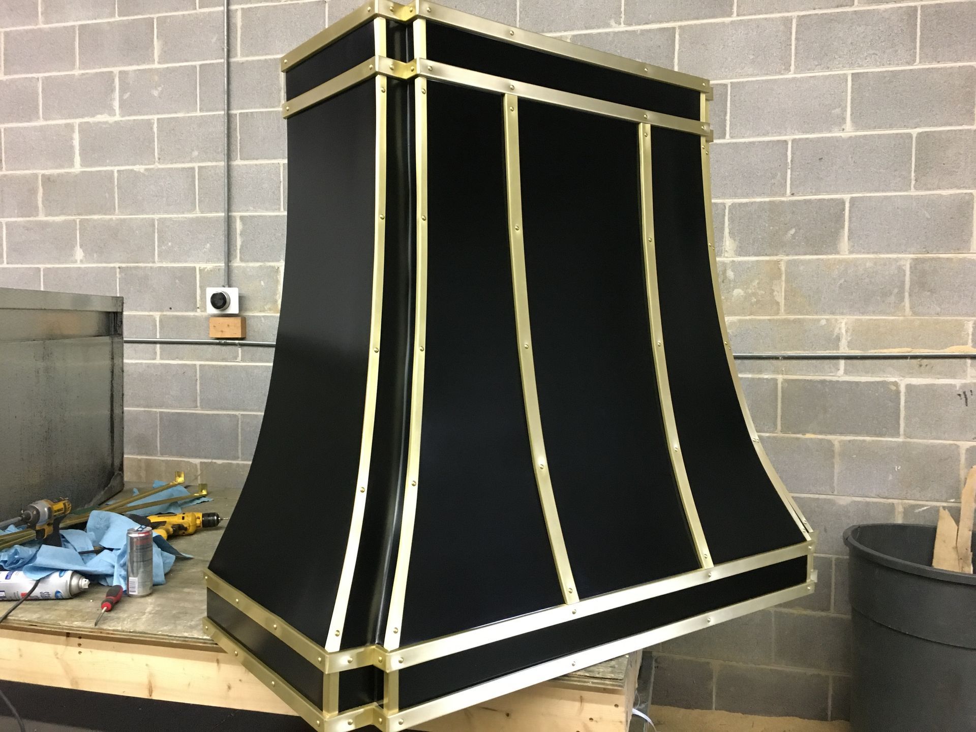 A black and gold lamp shade is sitting on a table in front of a brick wall