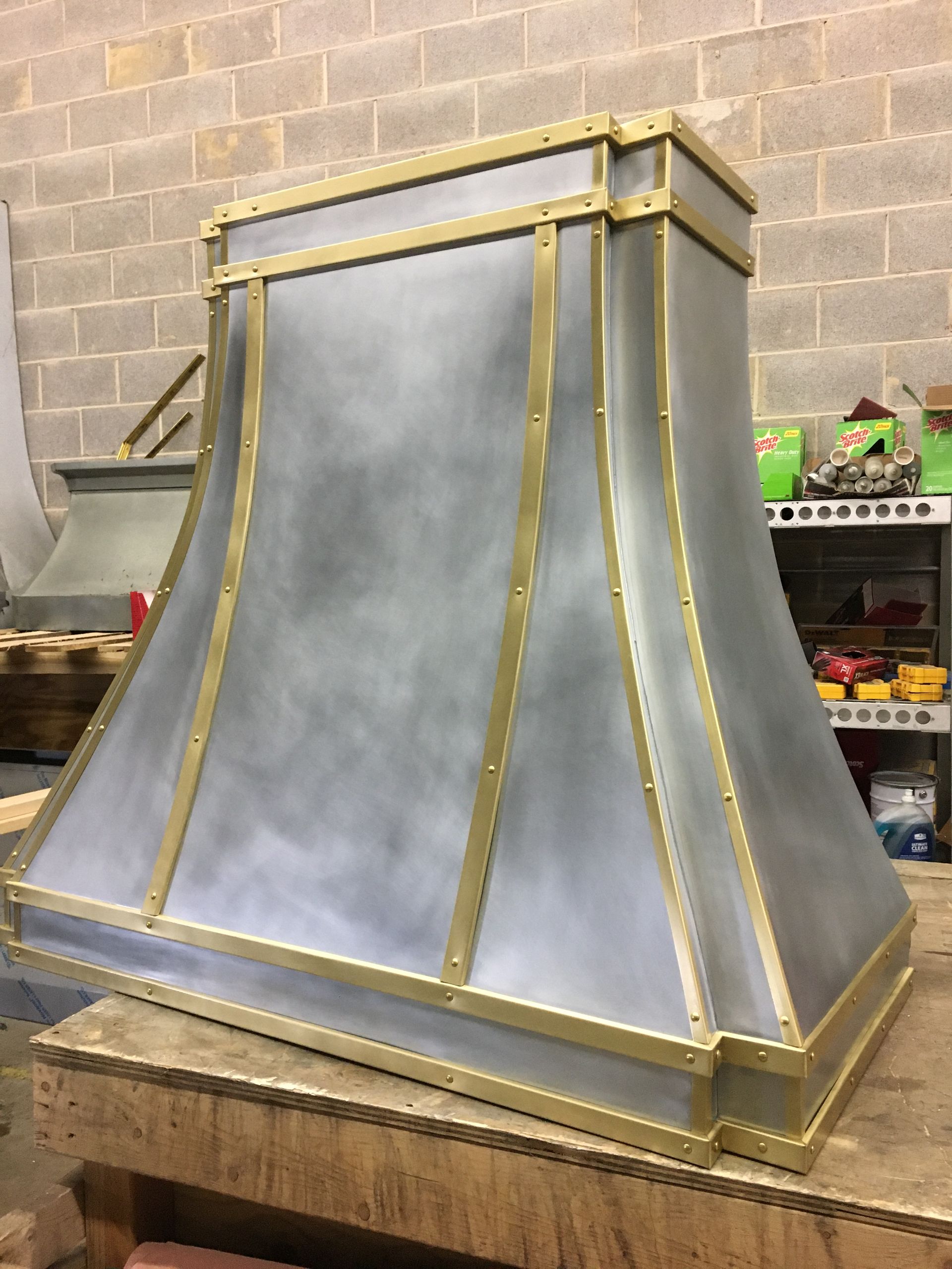 A metal hood with brass trim is sitting on a wooden table.