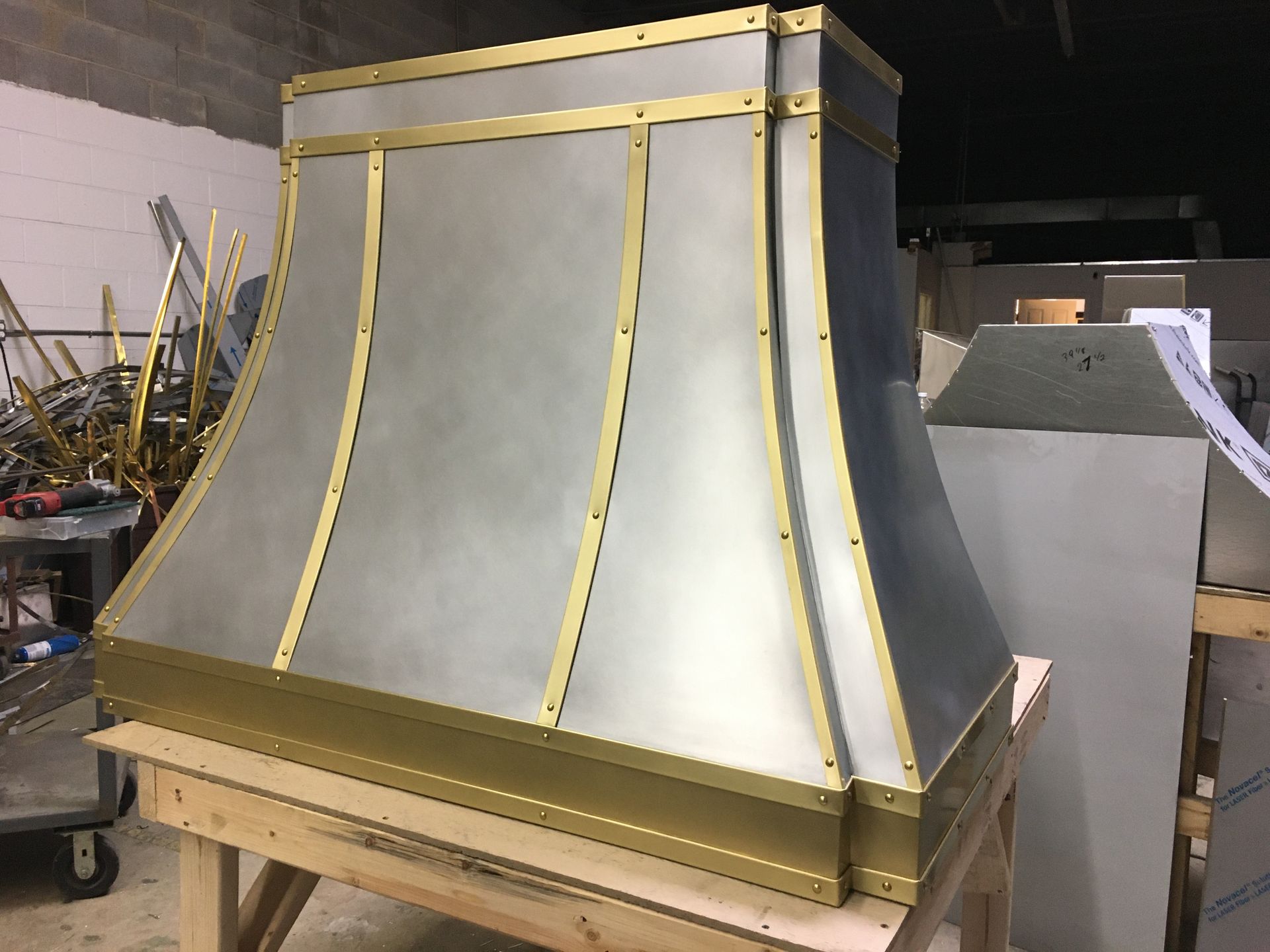 A metal hood with brass trim is sitting on a wooden table.