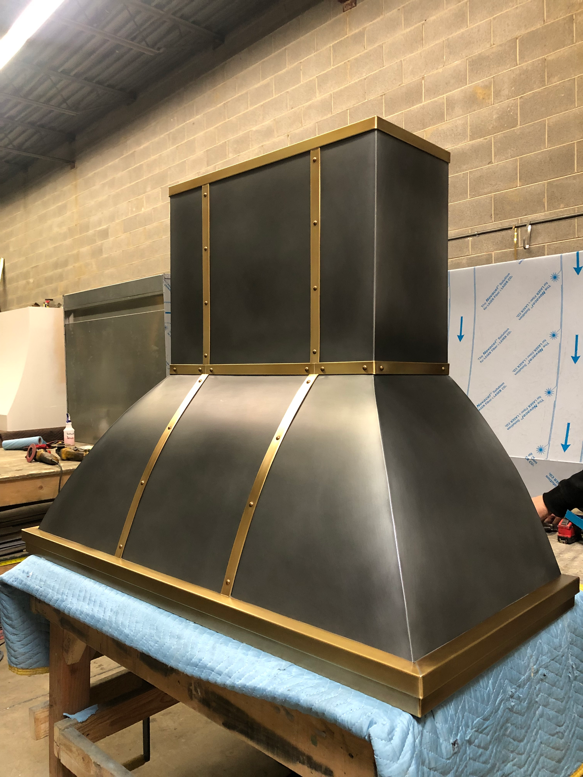 A stainless steel hood with brass trim is sitting on top of a wooden table.