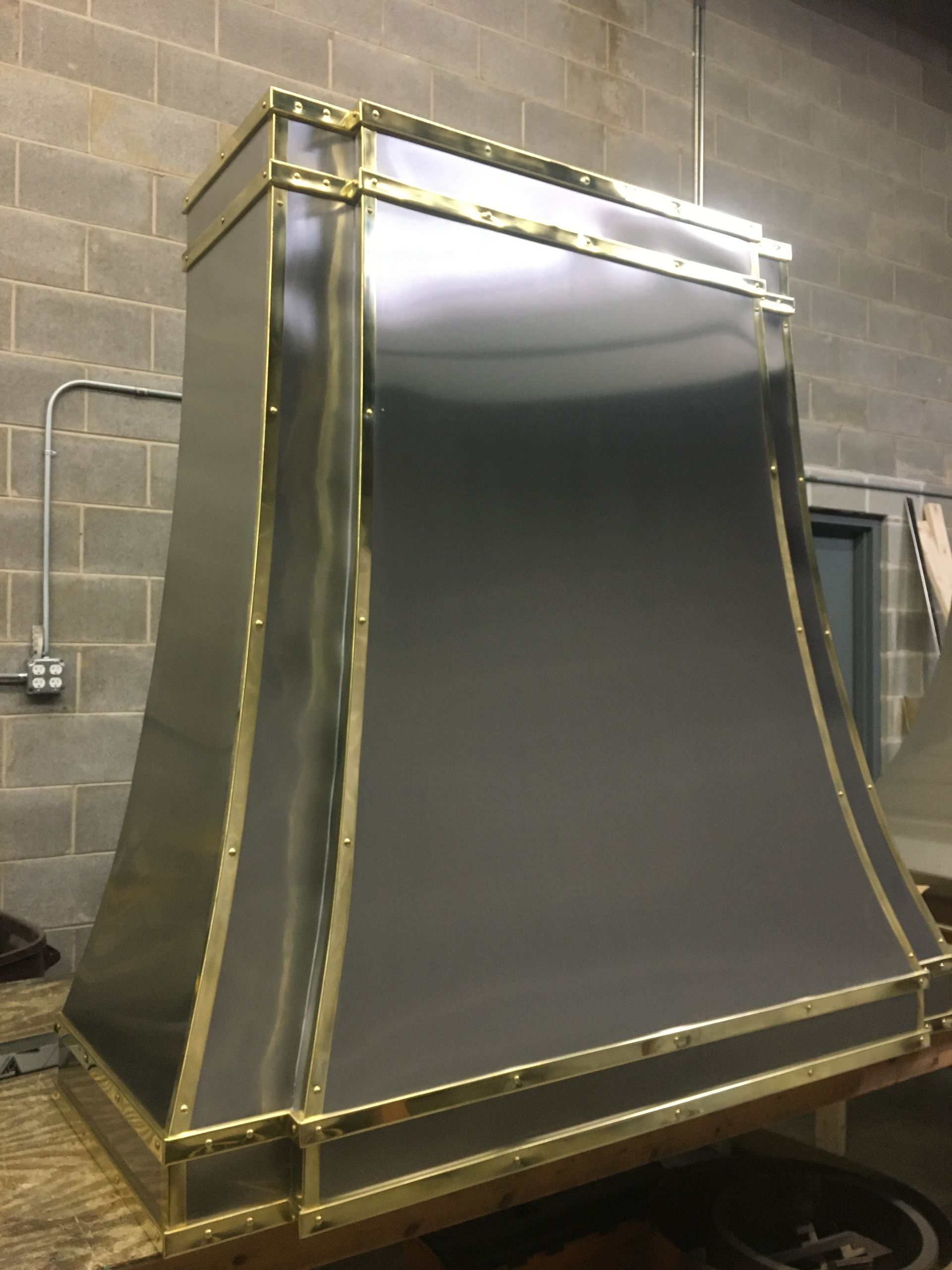 A stainless steel hood with gold trim is sitting on a wooden table.