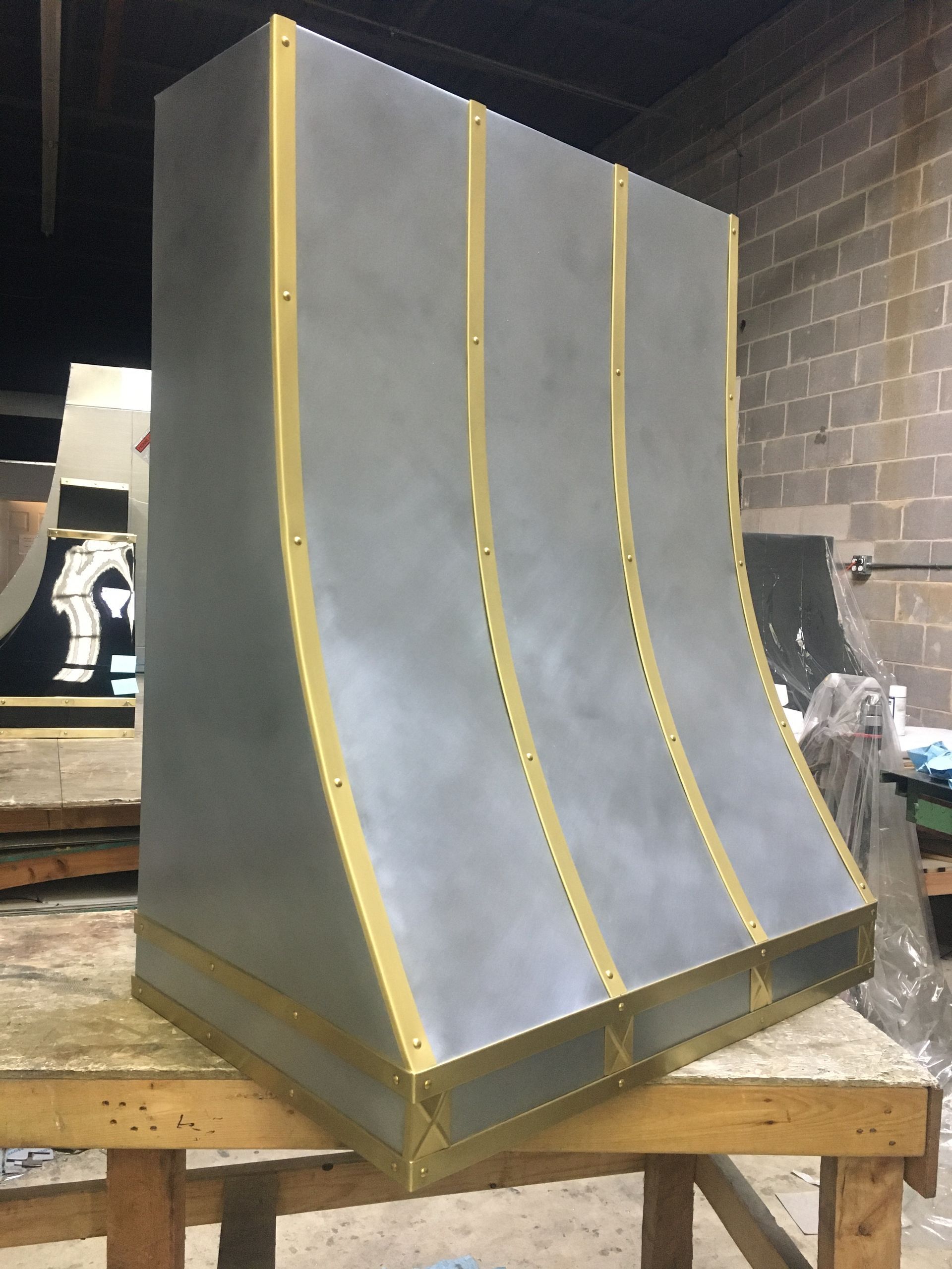 A stainless steel hood with gold trim is sitting on a wooden table.