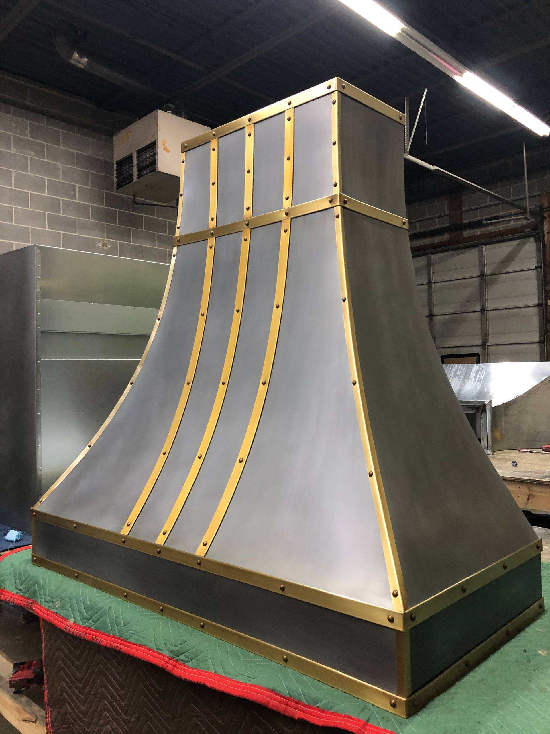 A stainless steel hood with gold trim sits on a table