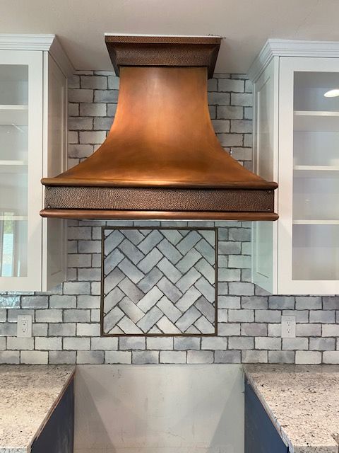 A kitchen with a copper hood and a herringbone tile wall.