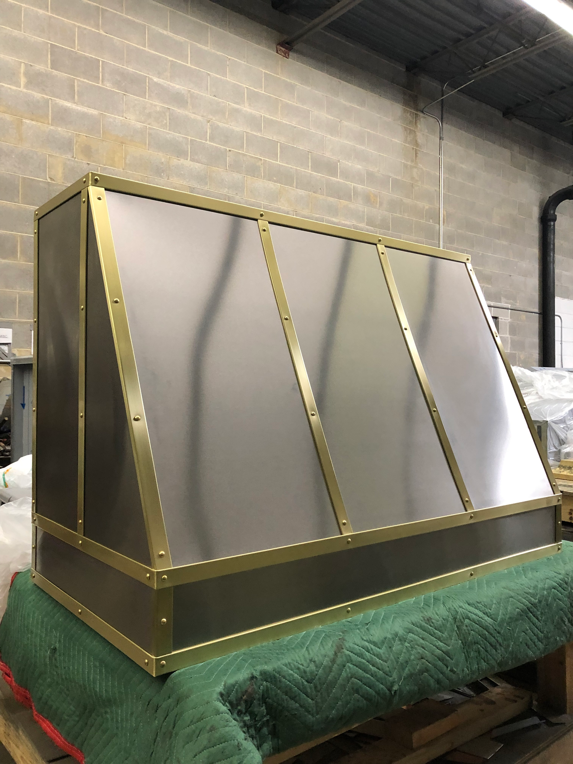 A stainless steel hood with brass trim is sitting on top of a green table.