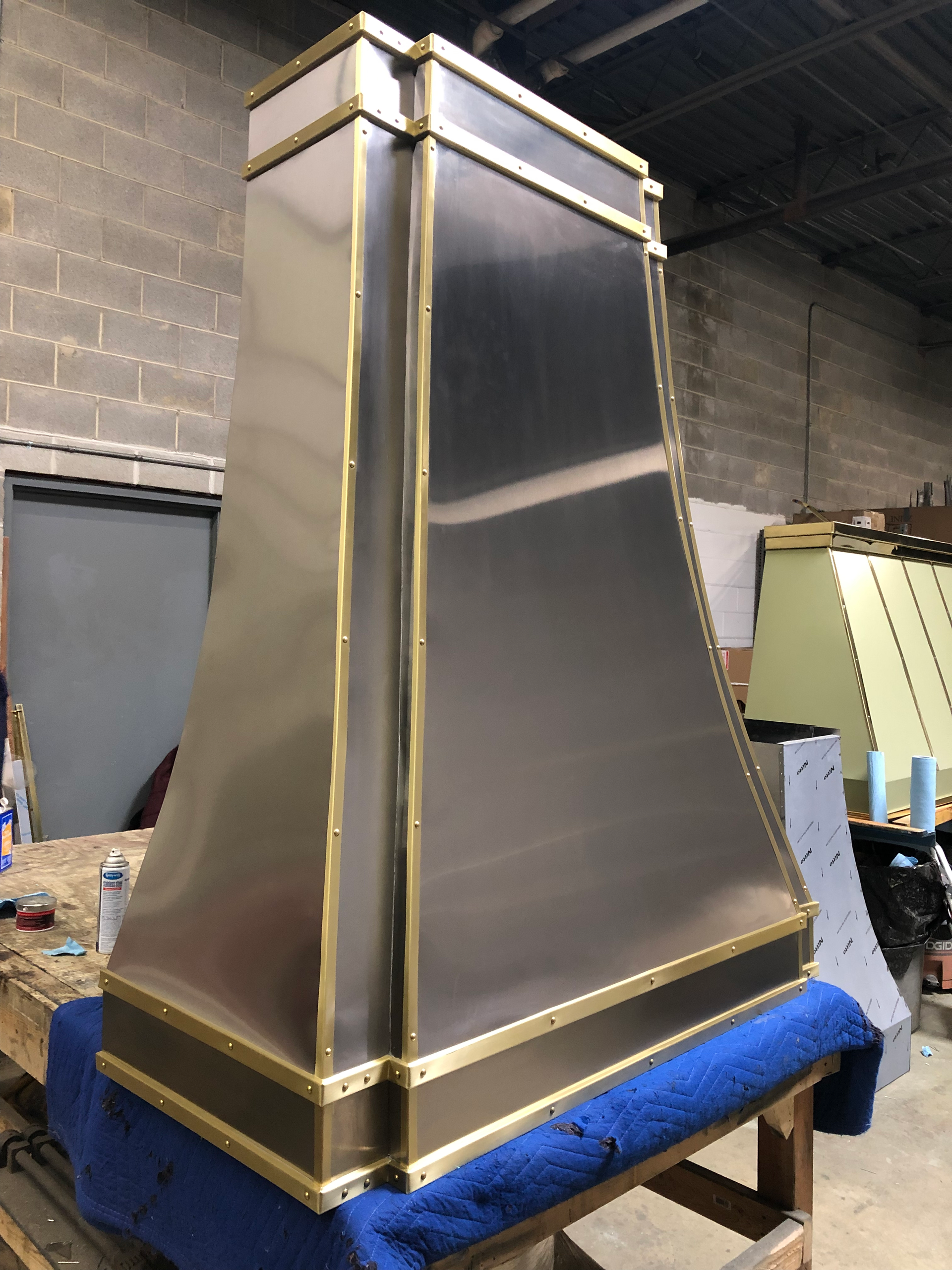 A stainless steel hood with brass trim sits on a wooden table