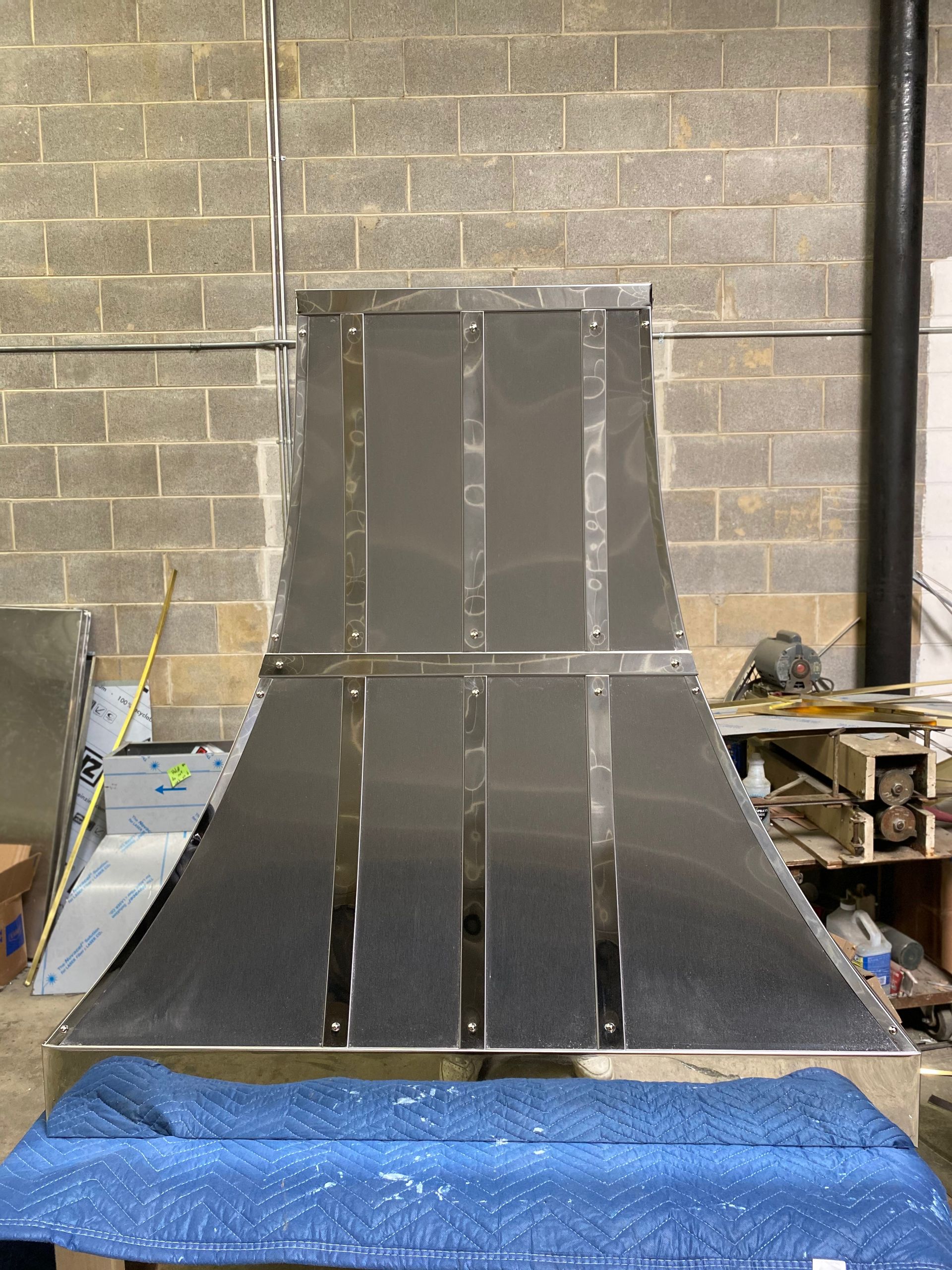 A large stainless steel hood is sitting on top of a blue table.