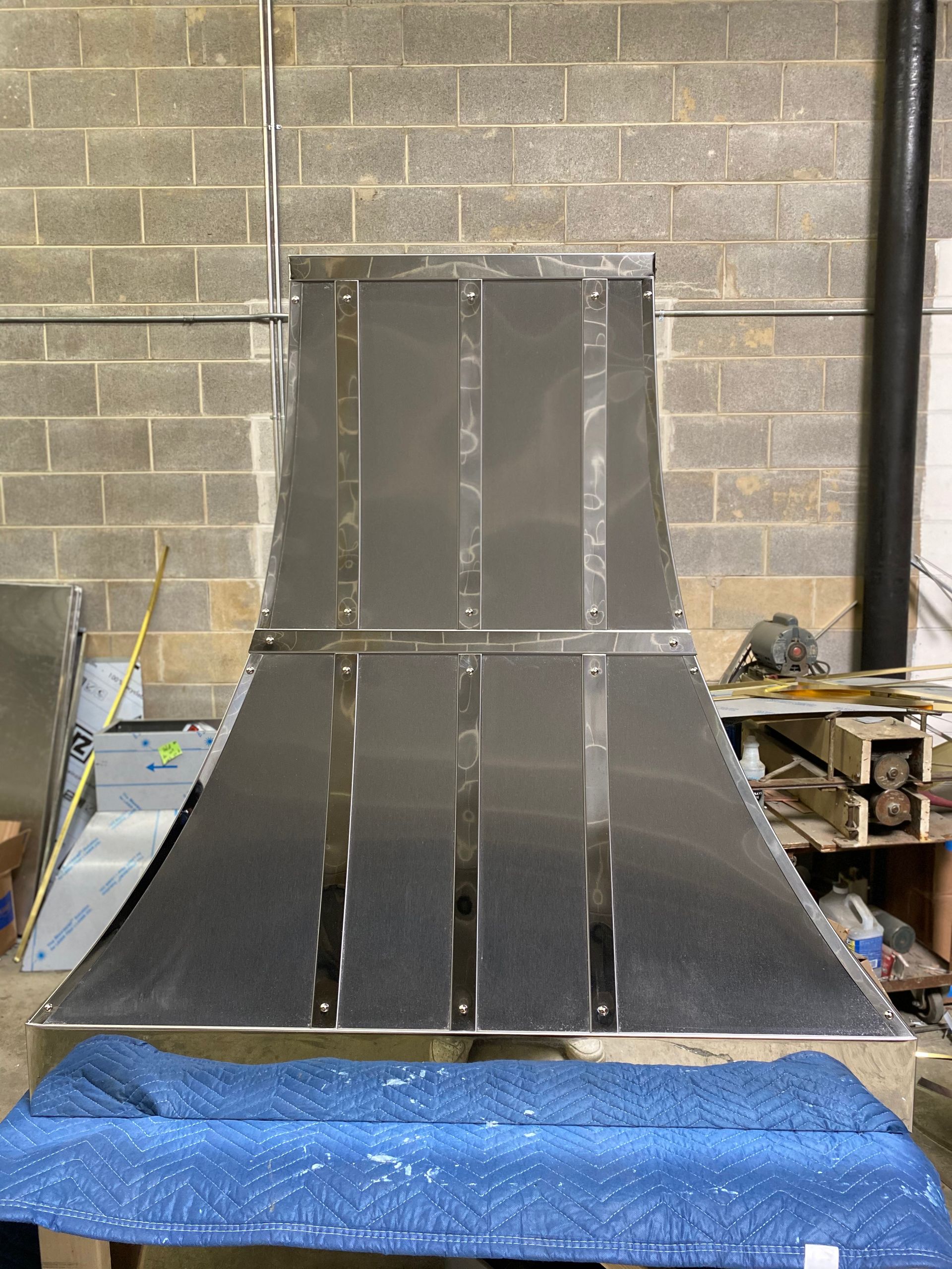 A stainless steel hood is sitting on top of a blue table.