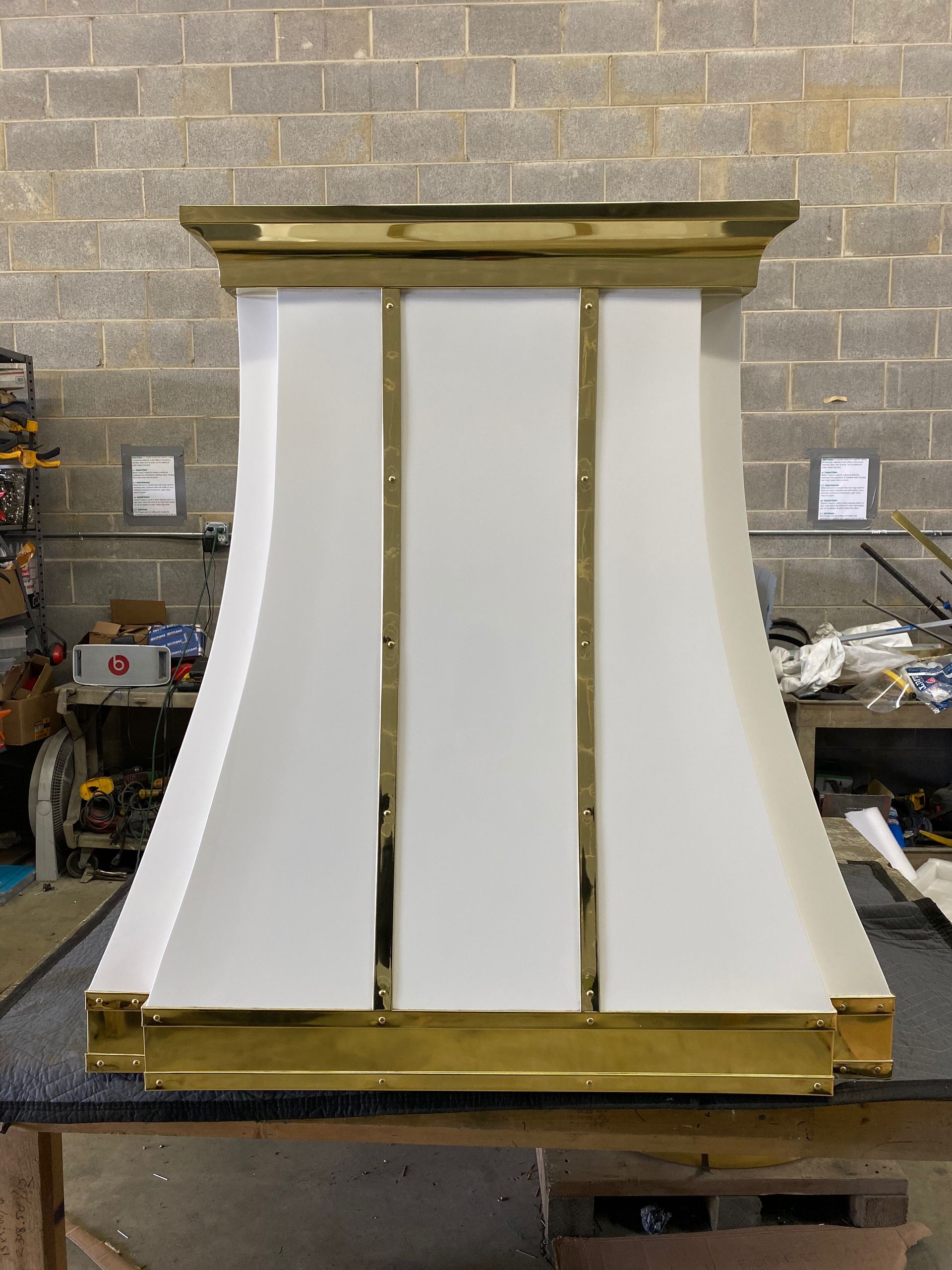 A white and gold lamp is sitting on a table in front of a brick wall.