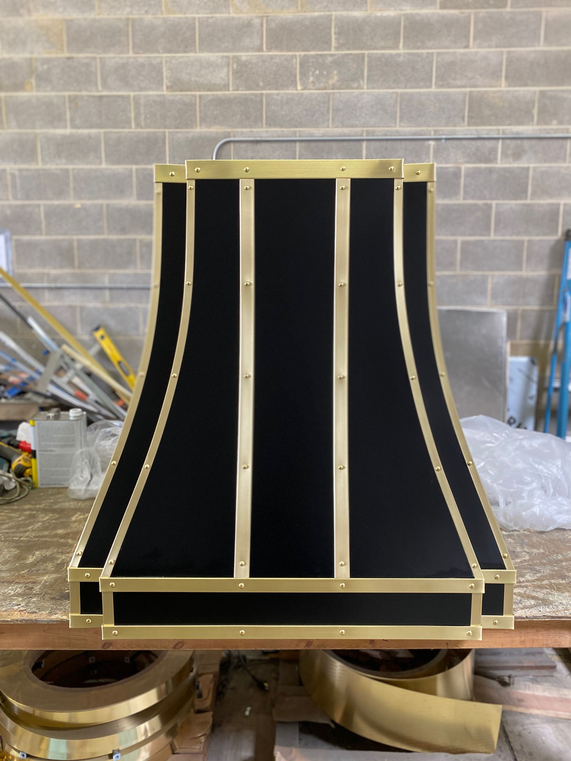 A black and gold lampshade is sitting on a table in front of a brick wall