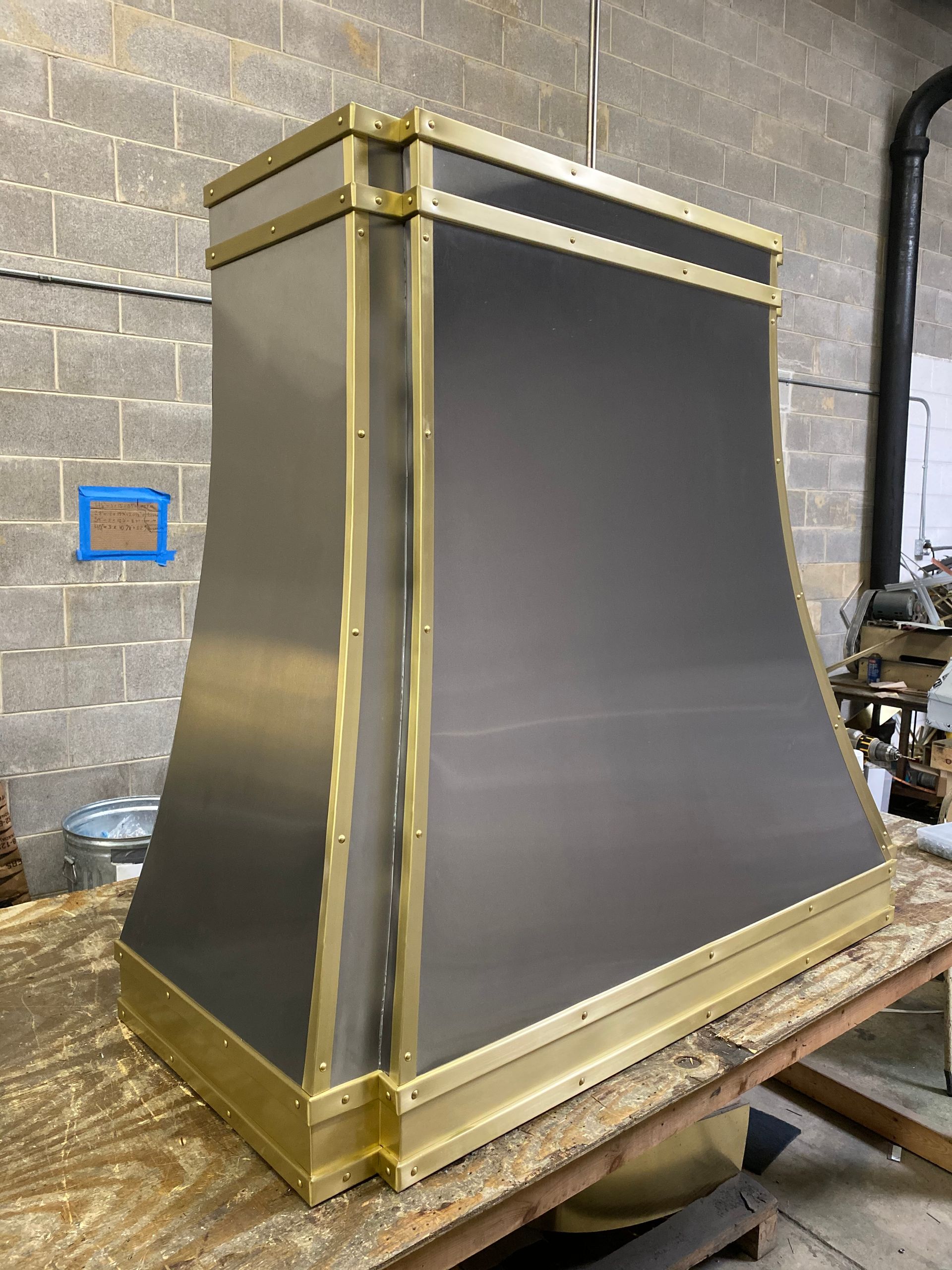 A stainless steel hood with brass trim is sitting on top of a wooden table.