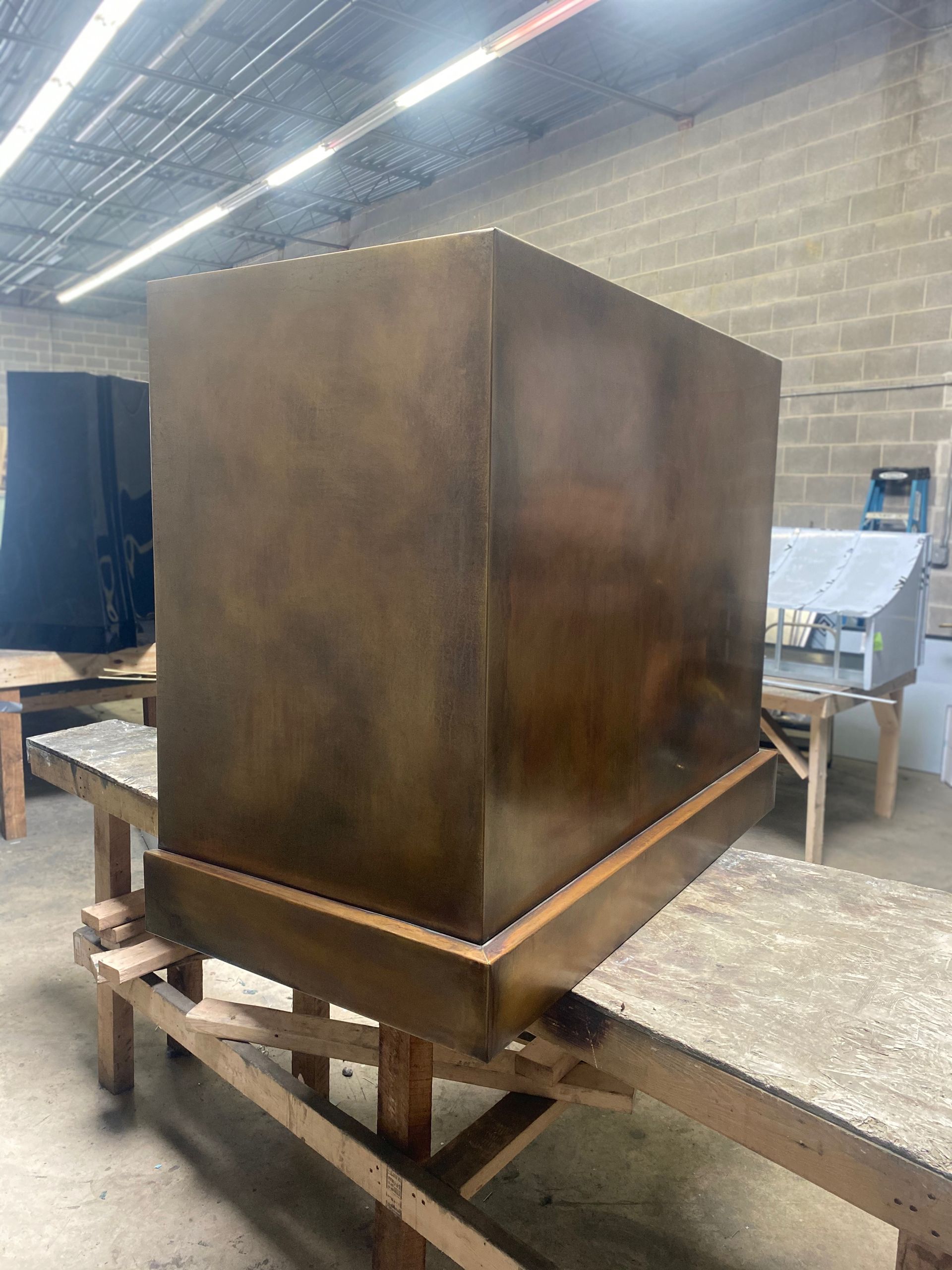 A large copper cube is sitting on top of a wooden table in a warehouse.