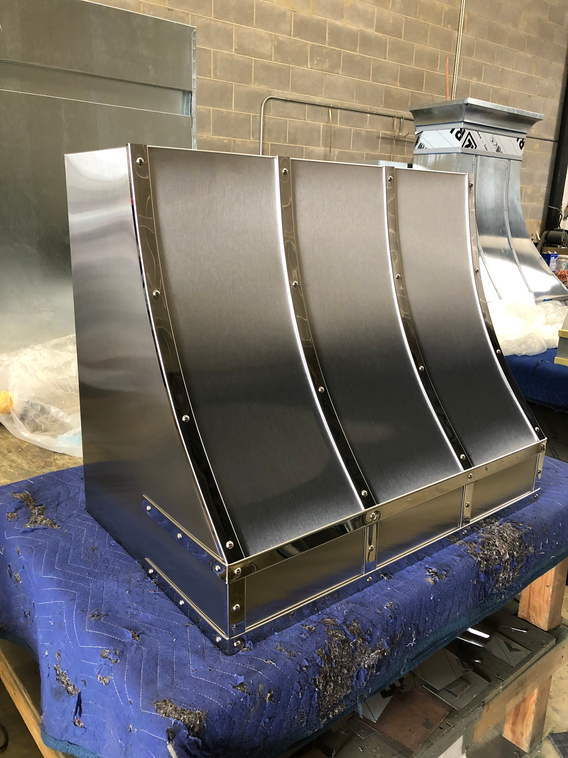 A stainless steel hood is sitting on top of a blue table.