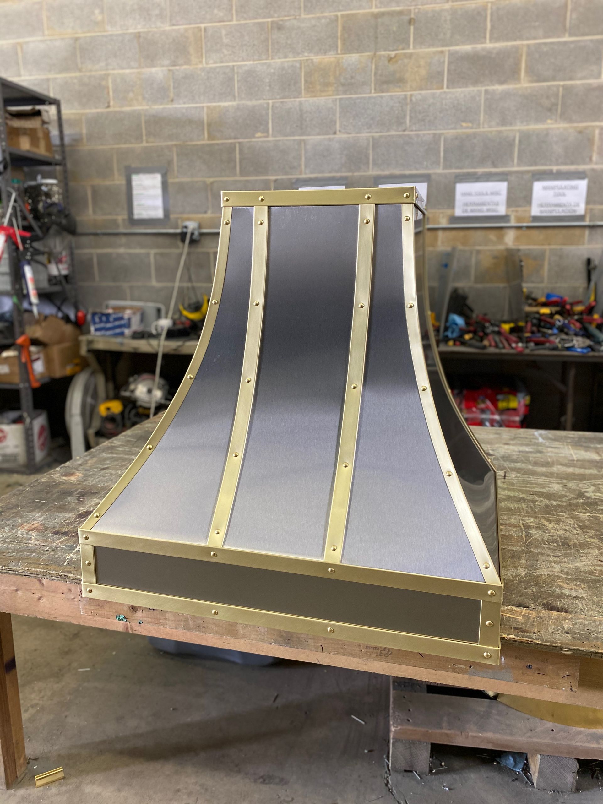 A stainless steel and brass hood is sitting on a wooden table.