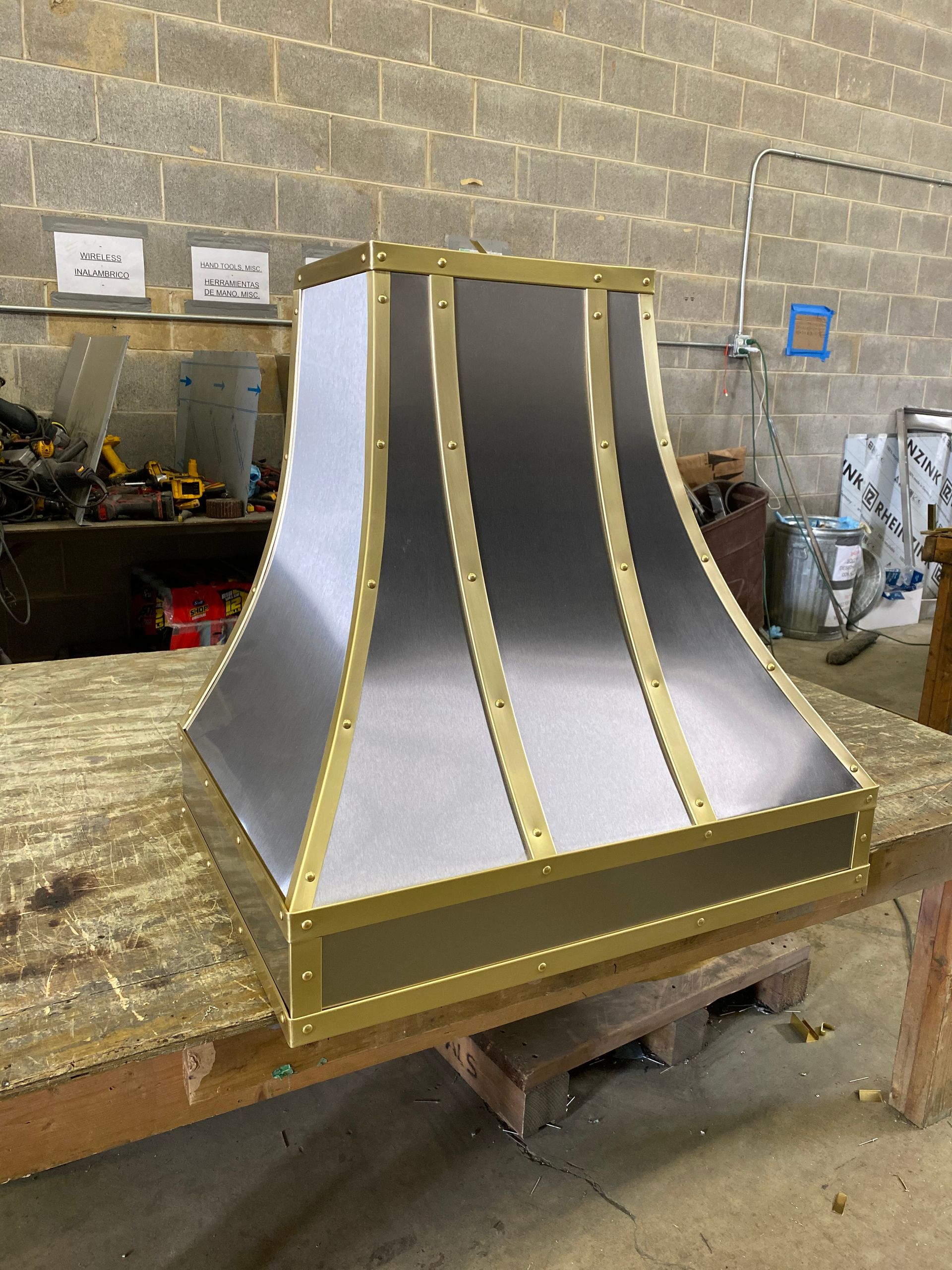 A stainless steel and brass hood is sitting on a wooden table.