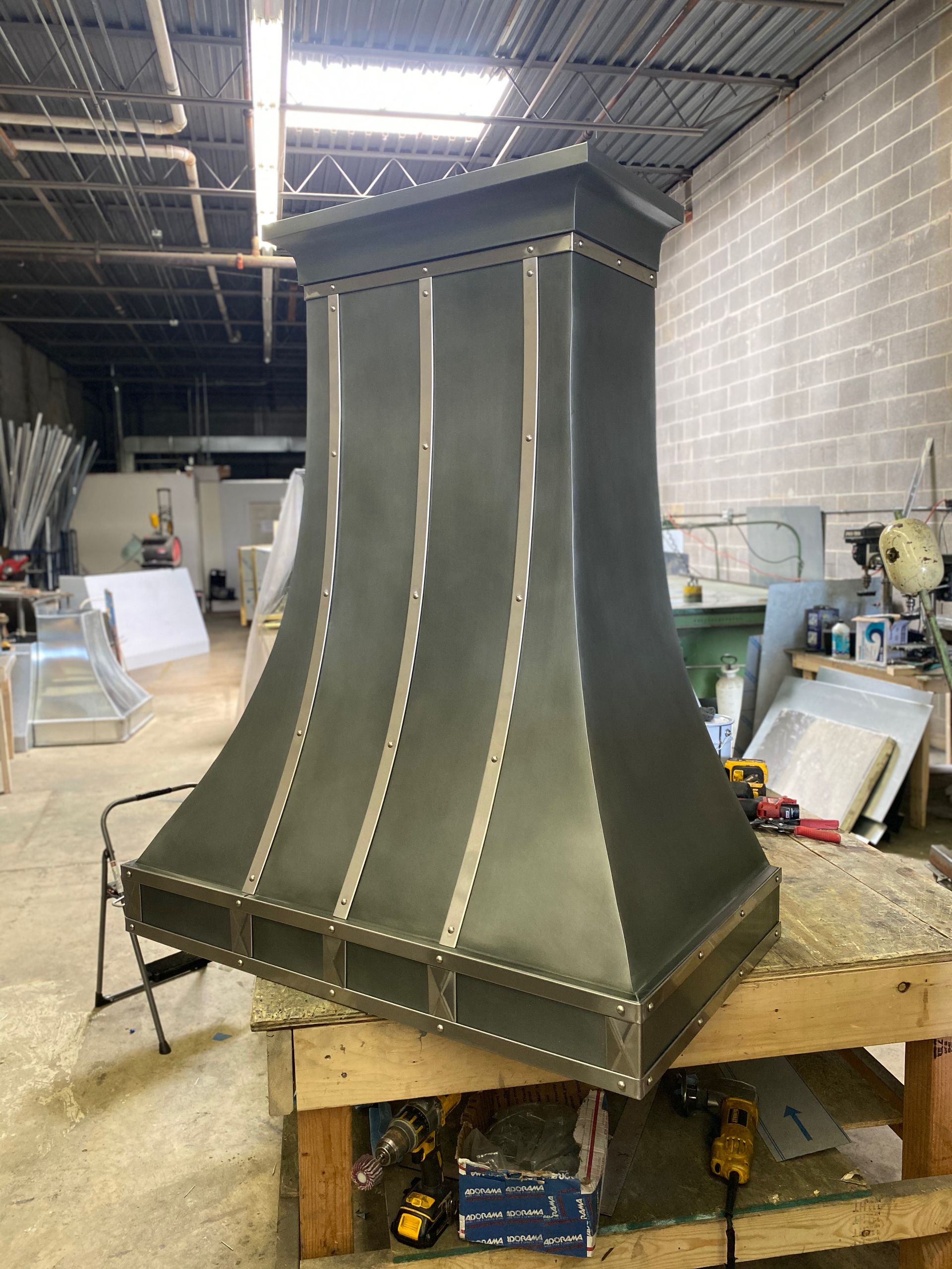 A metal hood is sitting on top of a wooden table in a warehouse.