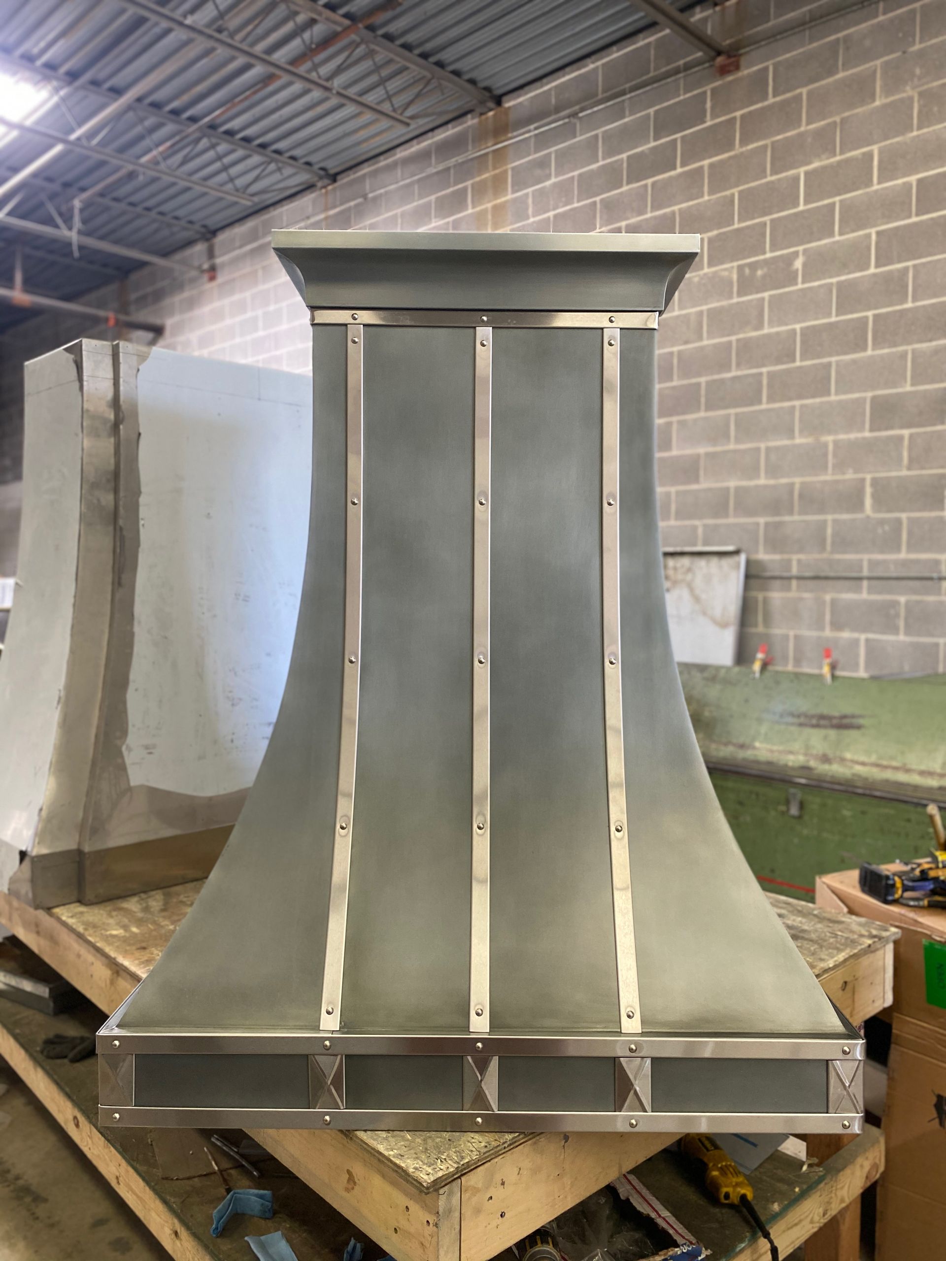 A stainless steel hood is sitting on top of a wooden table in a warehouse.