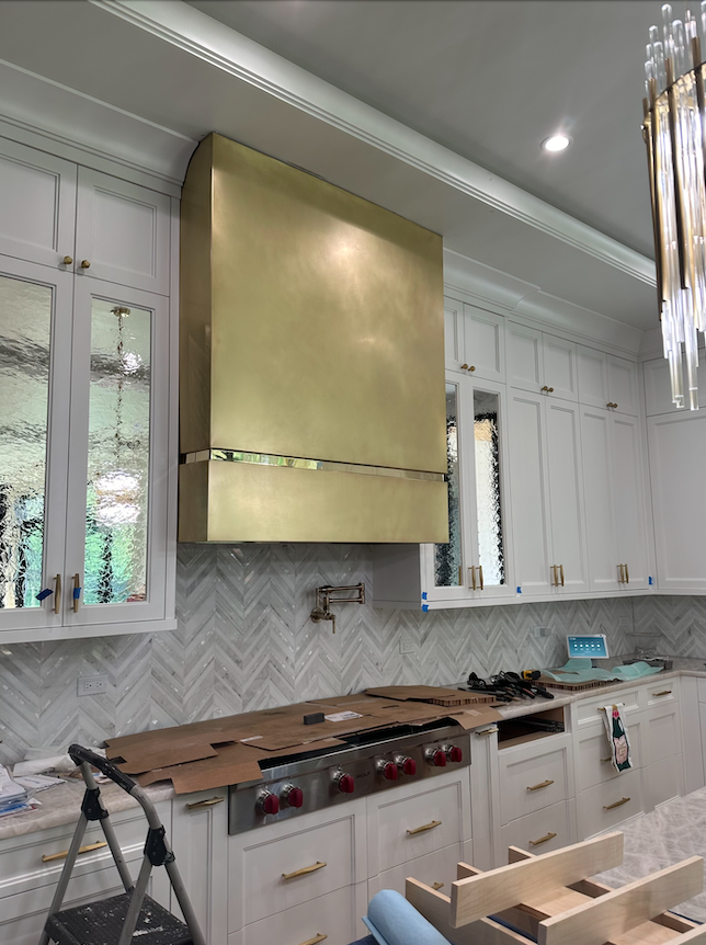A kitchen with white cabinets and a brass hood