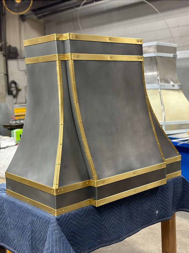 A stainless steel hood with gold trim is sitting on a table.