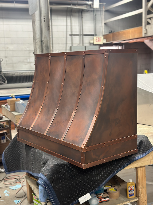 A copper hood is sitting on top of a wooden table.