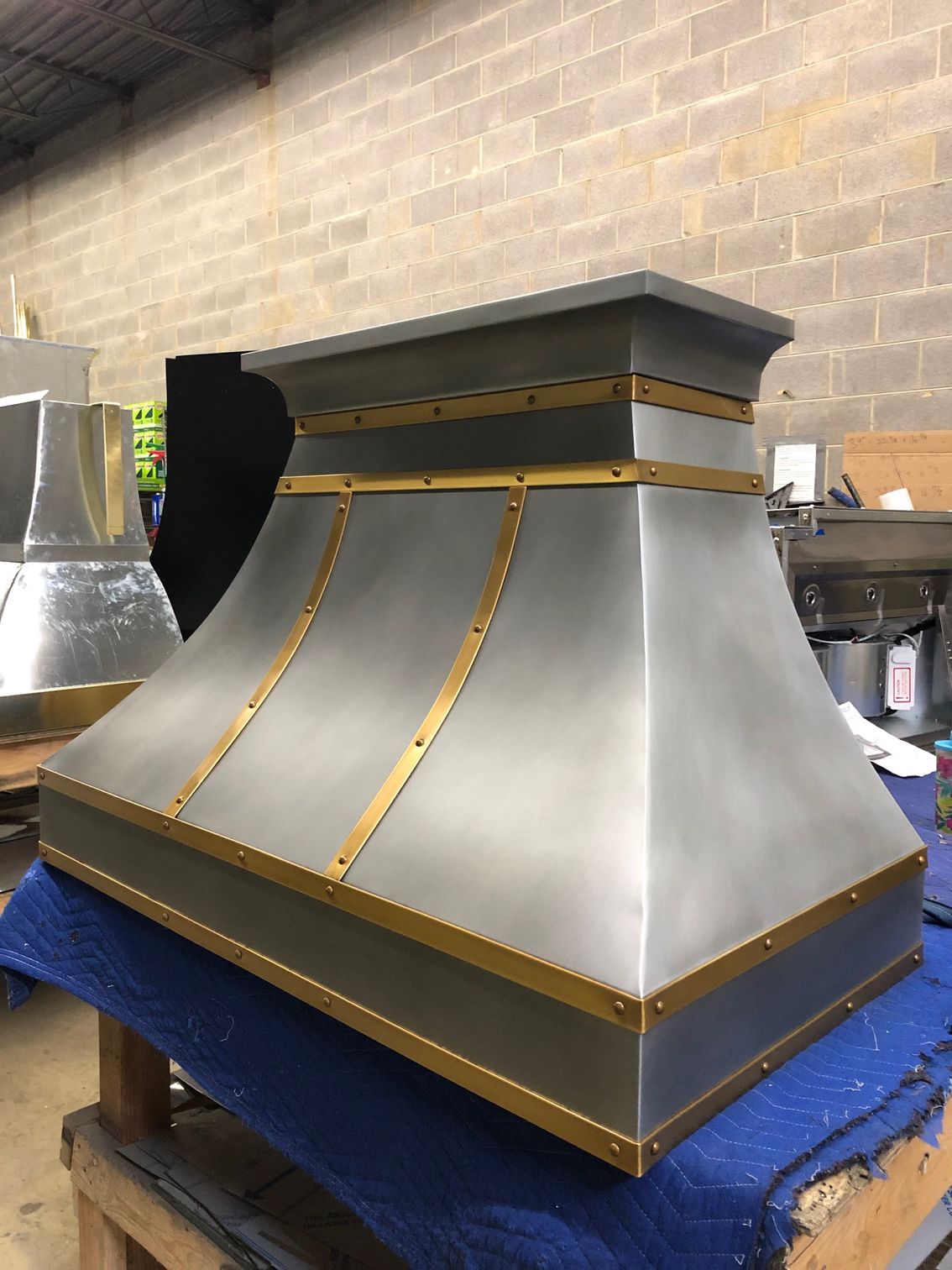 A stainless steel hood with brass trim is sitting on top of a blue table.