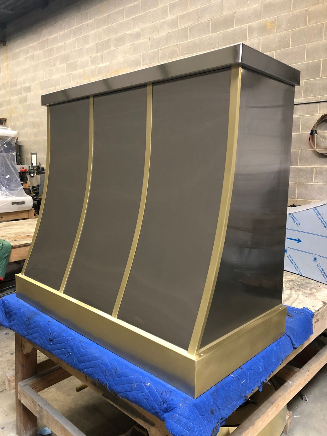 A stainless steel hood with brass trim is sitting on top of a wooden table.