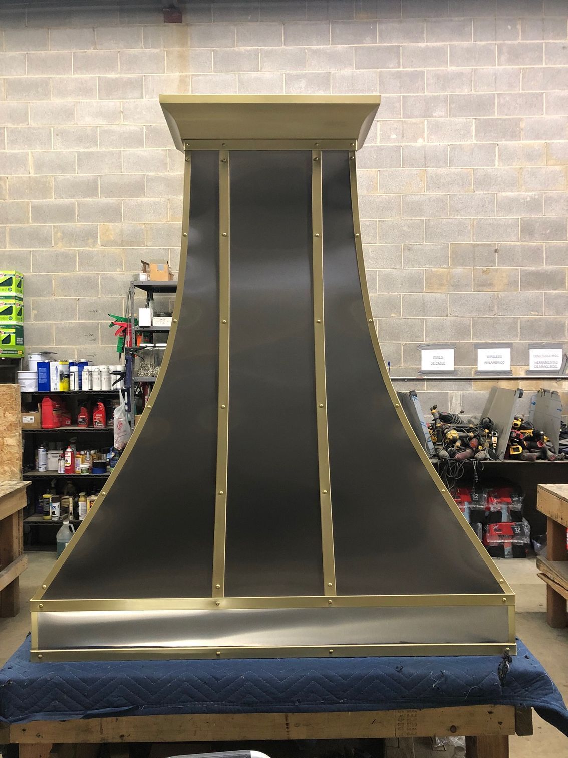 A stainless steel hood with brass trim is sitting on a wooden table.