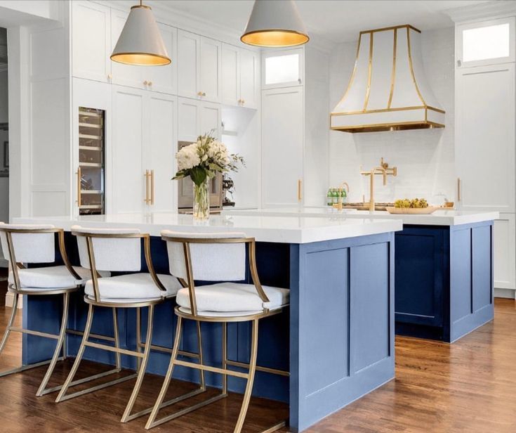 A kitchen with a blue island , white cabinets , and gold stools.