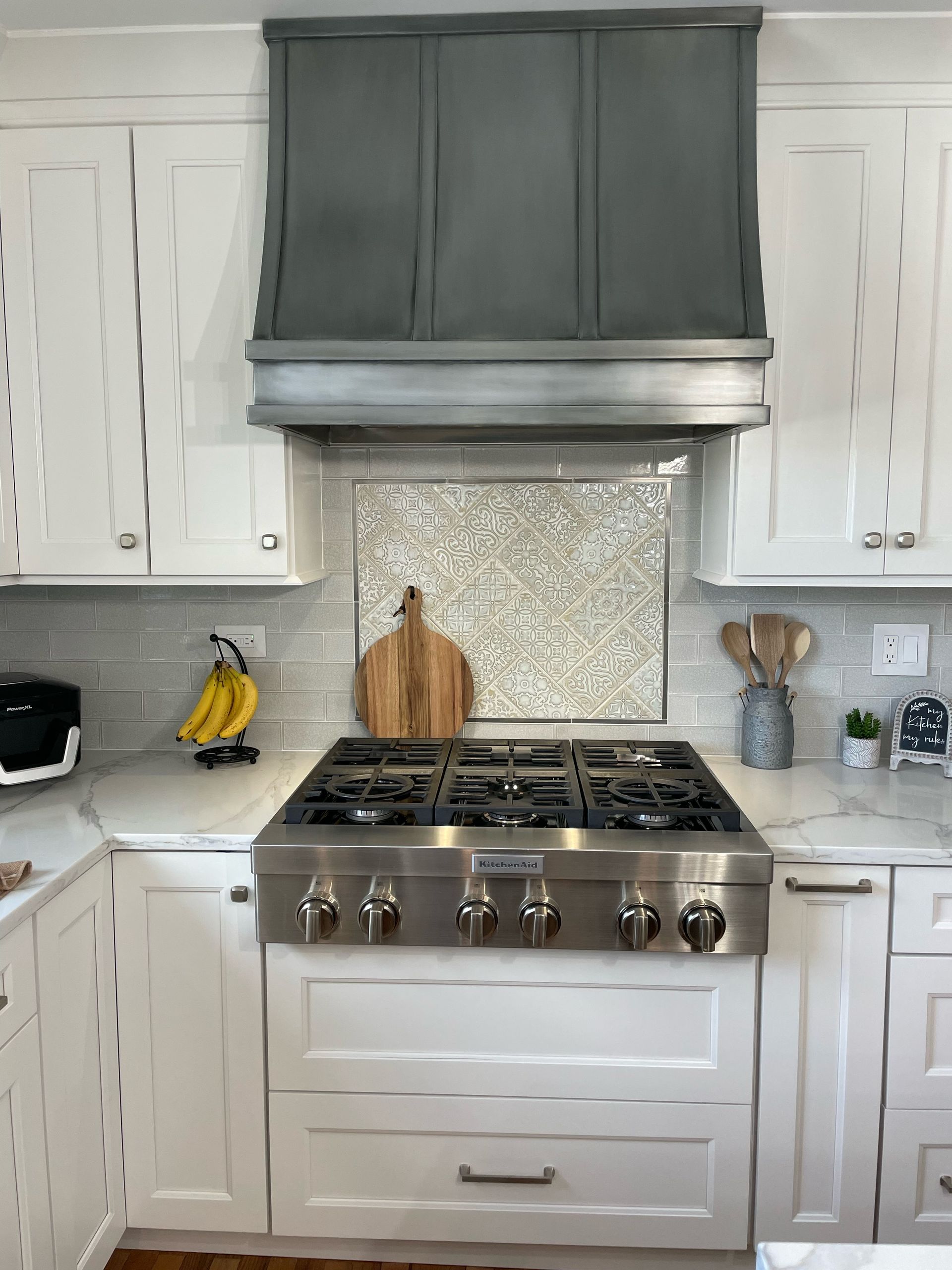 A kitchen with white cabinets and a stove with a hood above it.