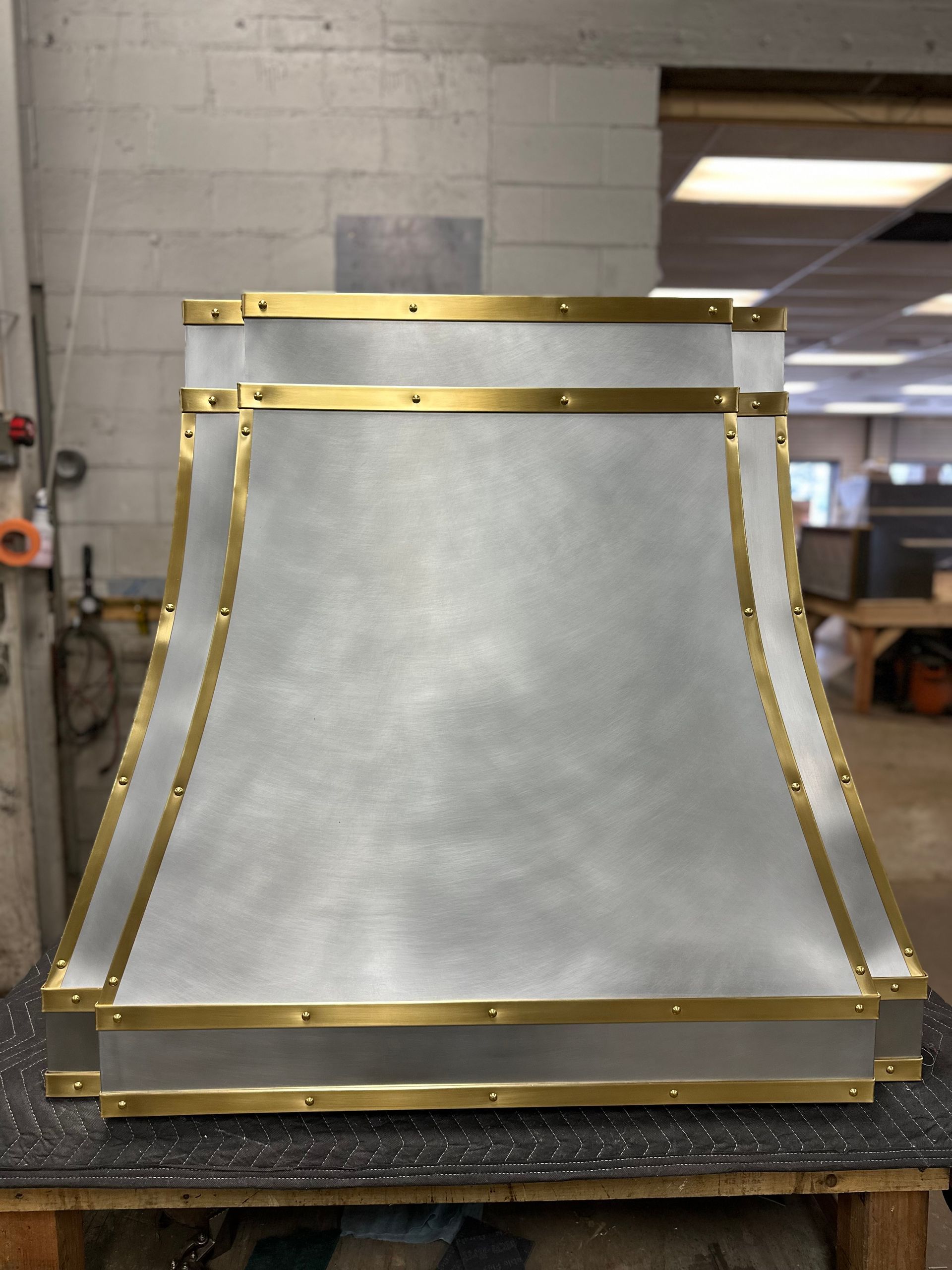 A metal hood with brass trim is sitting on a wooden table.