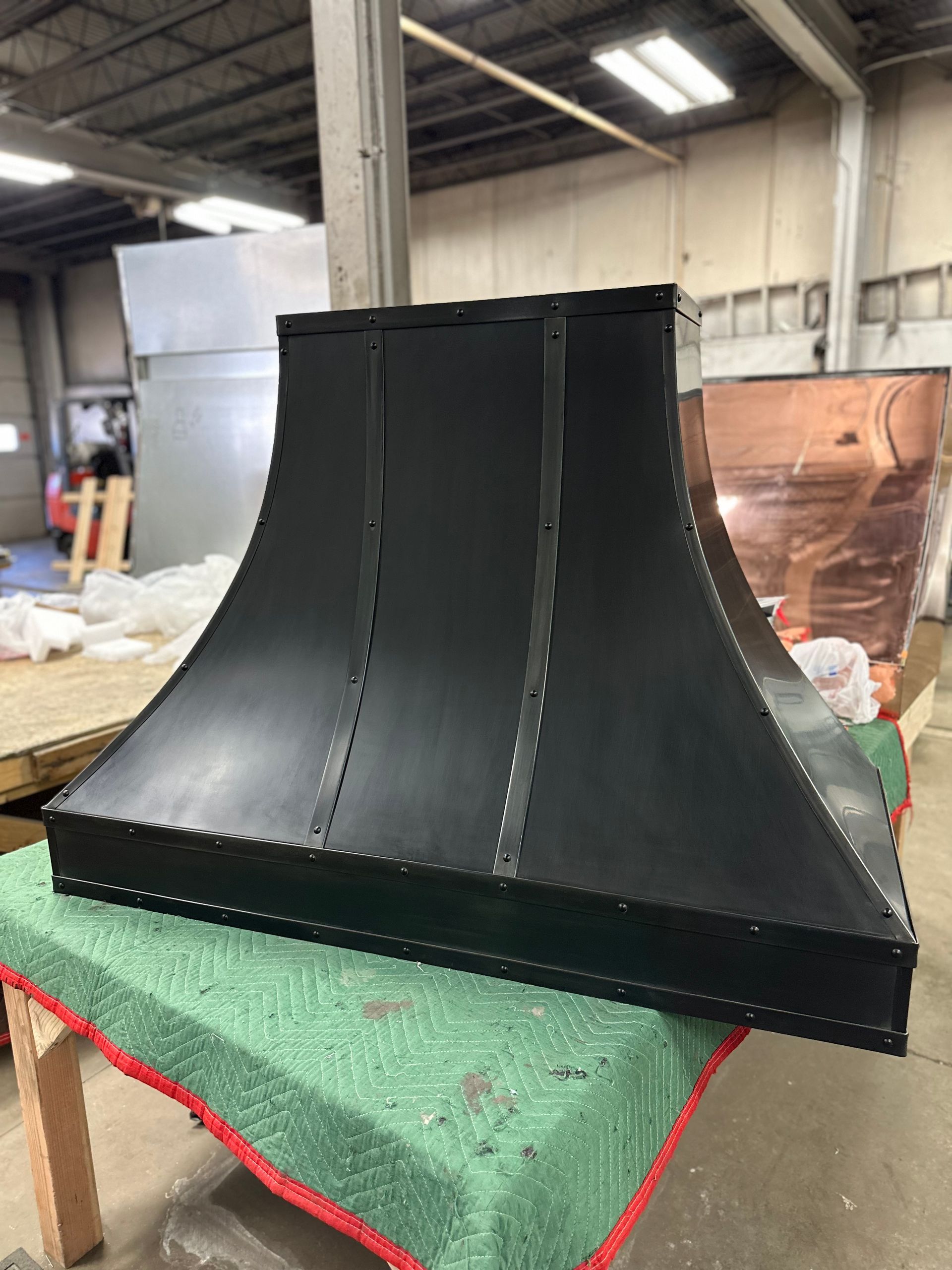 A black hood is sitting on top of a green table in a warehouse.